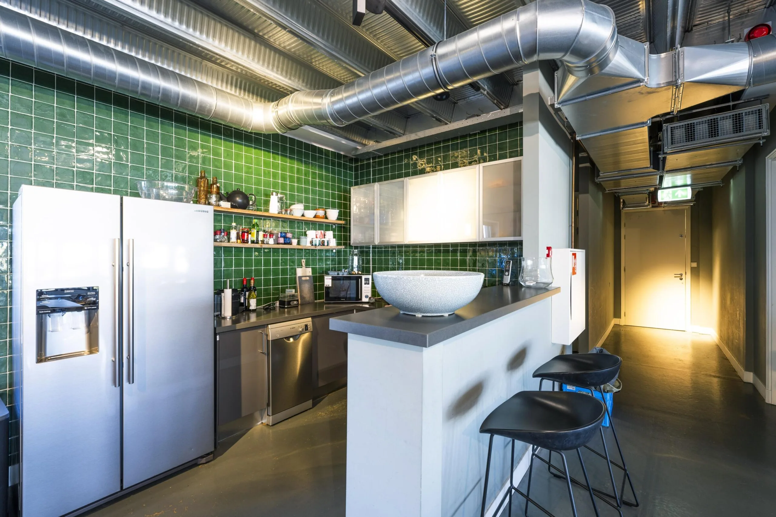 Modern industrial kitchen with green tiled walls, stainless steel appliances, and exposed ventilation ducts on Helicopterstraat.