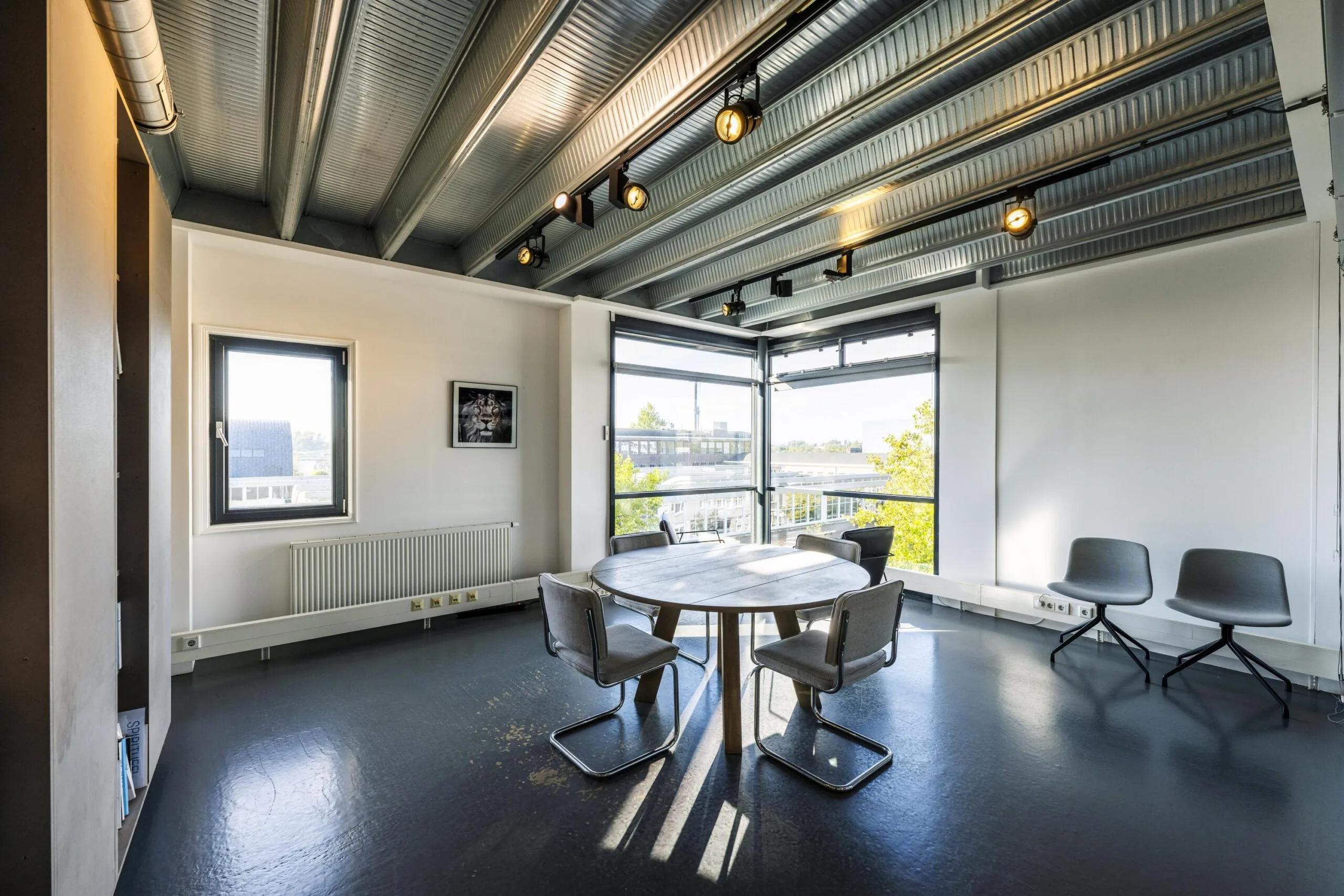 Modern meeting room with a round table, industrial ceiling, and large windows overlooking Helicopterstraat.