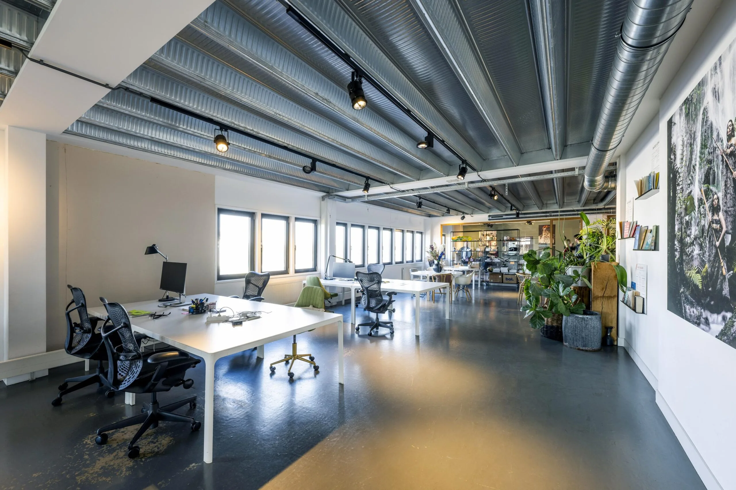 Modern open-plan office space on Helicopterstraat with shared desks, ergonomic chairs, and industrial ceiling design.