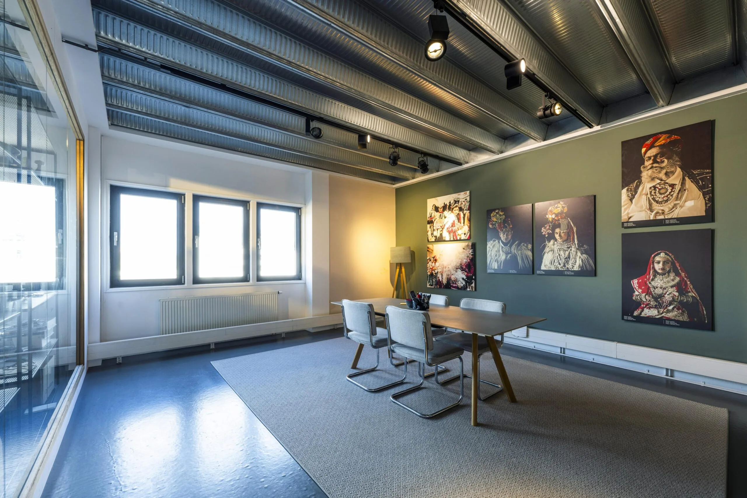 Modern meeting room on Helicopterstraat with industrial ceiling, large windows, and colorful cultural portraits on the wall.