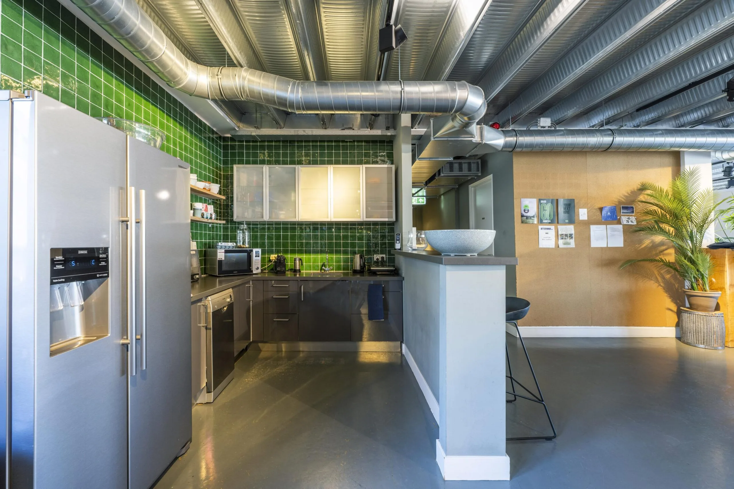Modern office kitchen at Helicopterstraat with green tiled walls, stainless steel appliances, and industrial-style exposed ductwork.
