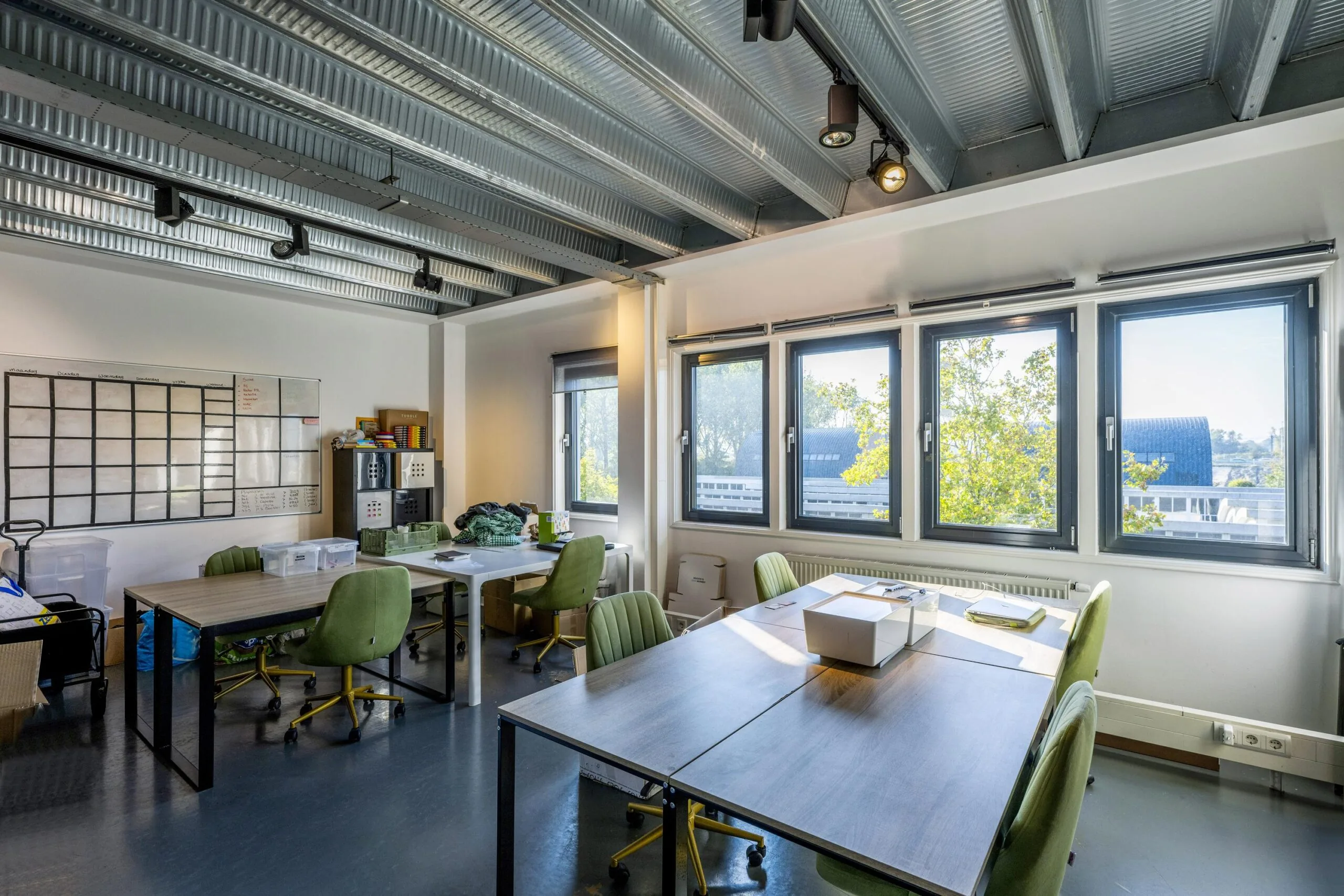 Bright office space on Helicopterstraat with multiple desks, green swivel chairs, large windows, and a visible whiteboard.