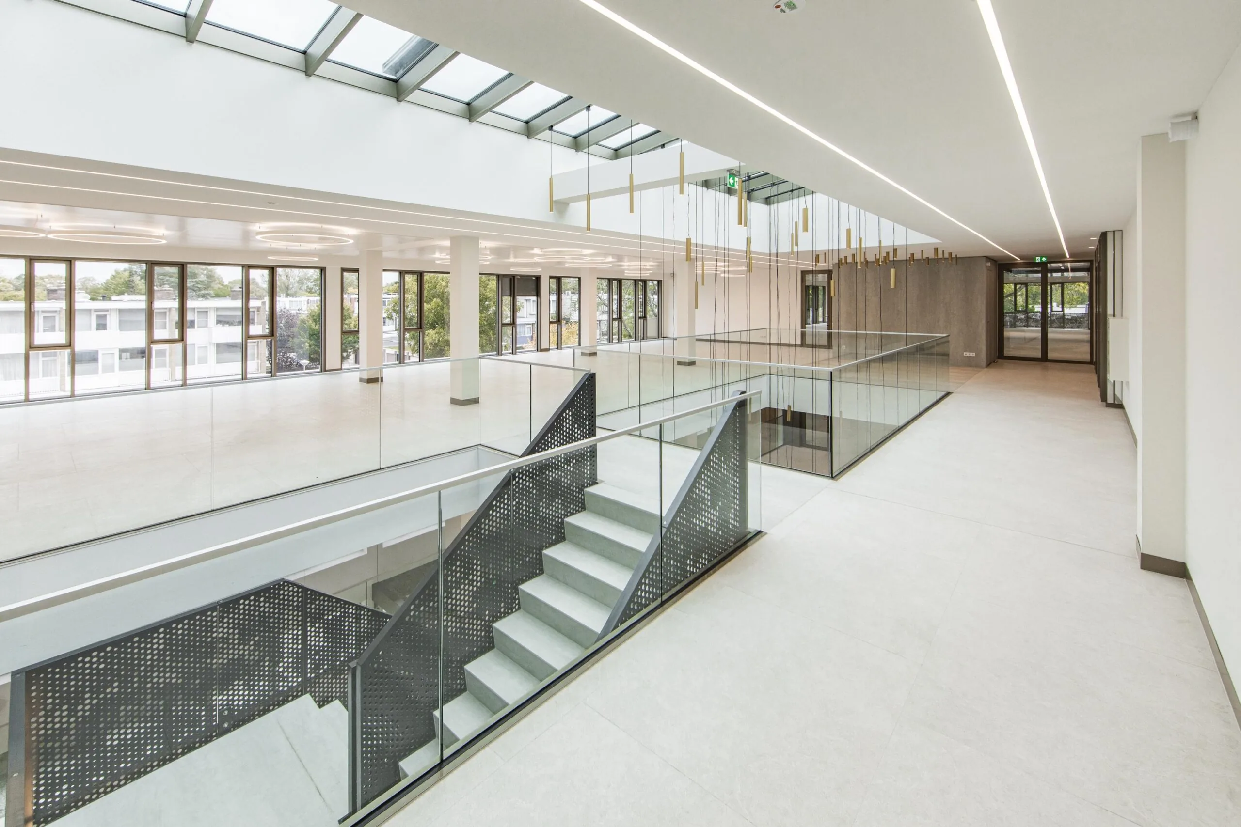 Modern interior of the Walborg building with large windows, a central staircase, and a glass balustrade under a skylight.