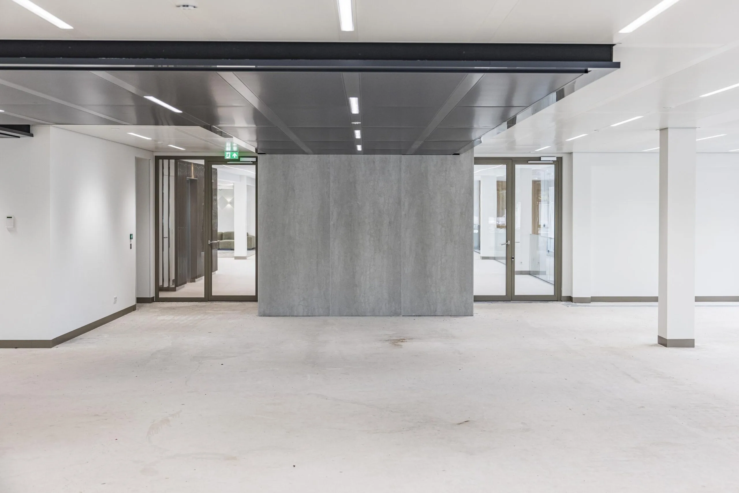 Empty modern office space with concrete flooring, glass doors, and a central grey wall partition.