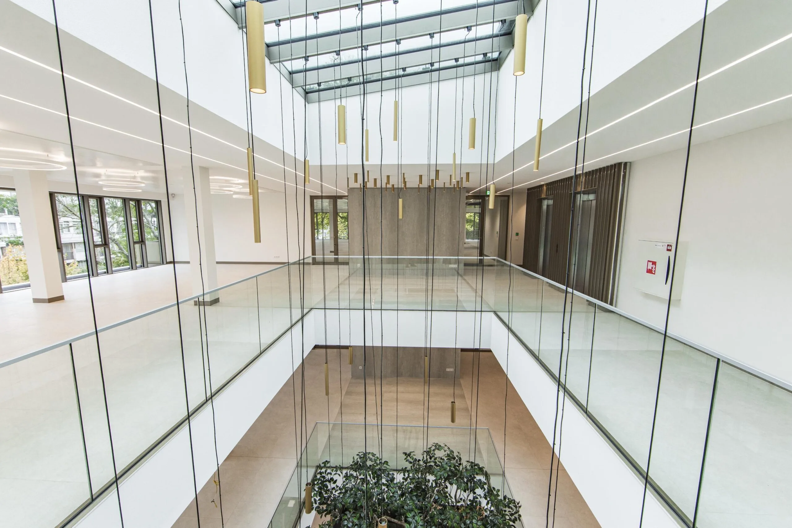 Modern open atrium of the Walborg building featuring glass railings, hanging pendant lights, and a skylight ceiling.