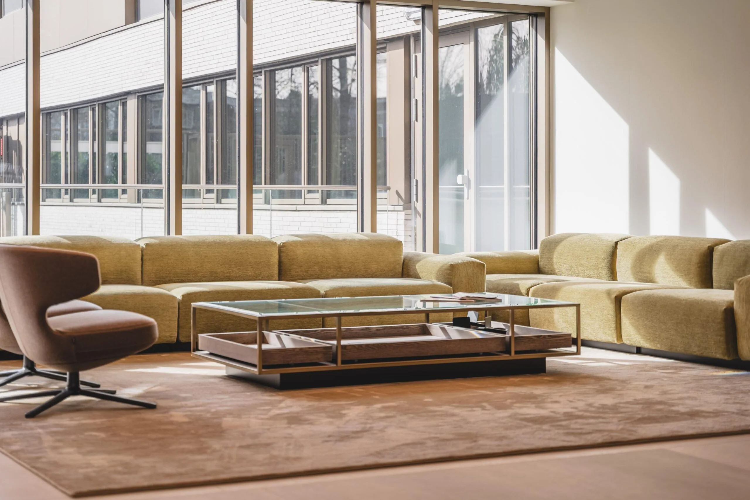 Modern lounge area with large yellow sectional sofa, glass coffee table, and floor-to-ceiling windows at Walborg.