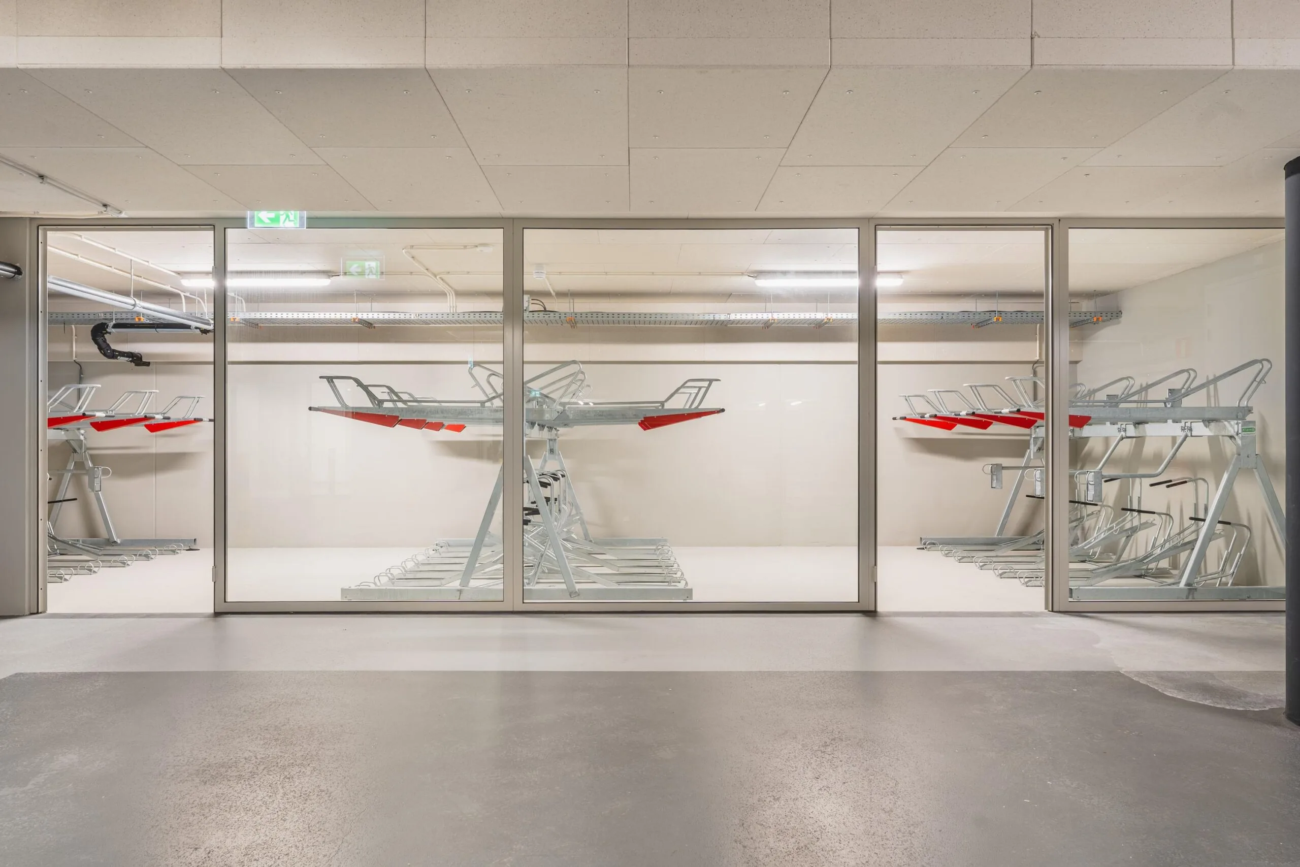 Indoor bicycle storage room with empty double-decker bike racks behind a glass wall.