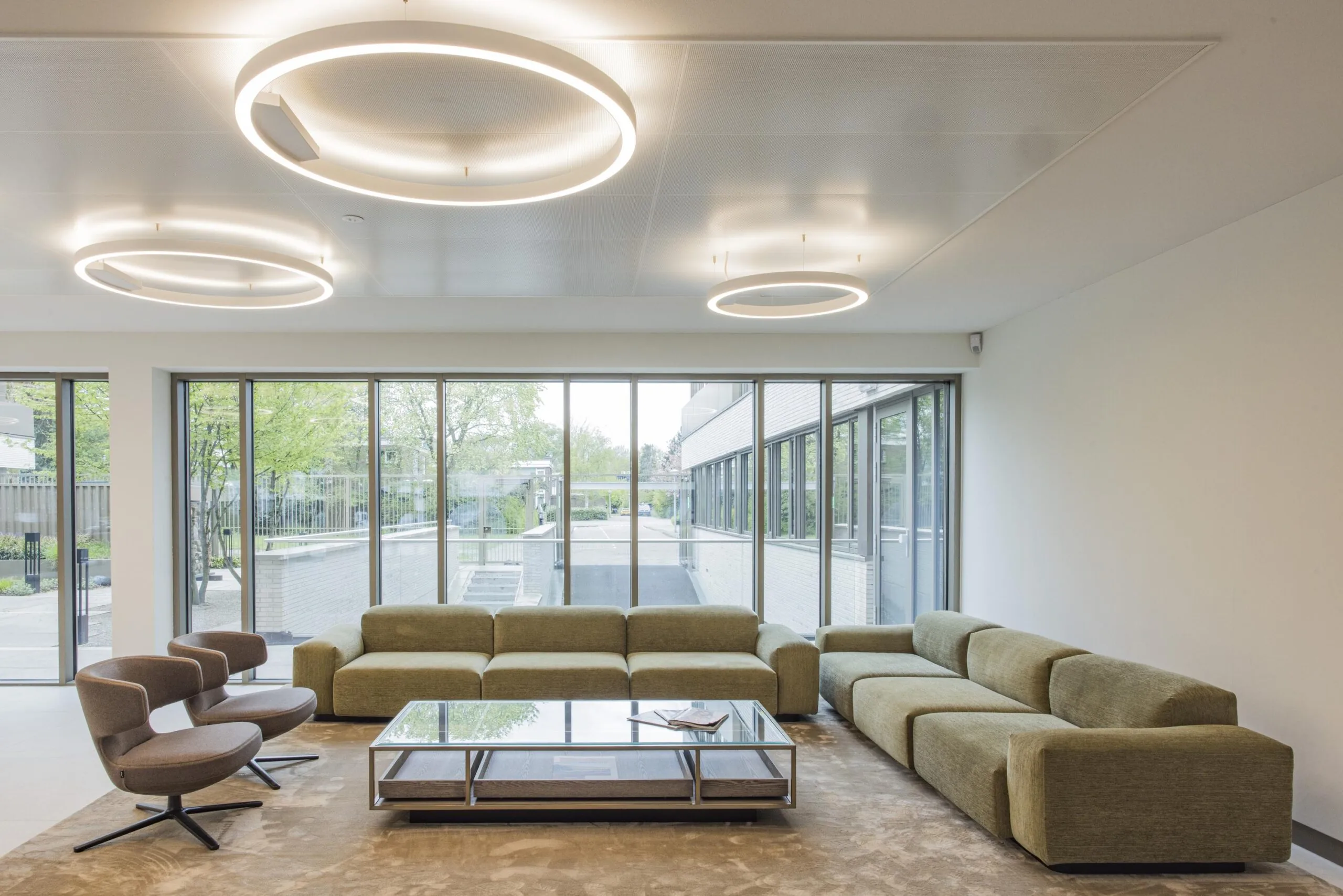 Modern lounge area in the Walborg building with green modular sofas, contemporary armchairs, large windows, and circular ceiling lights.