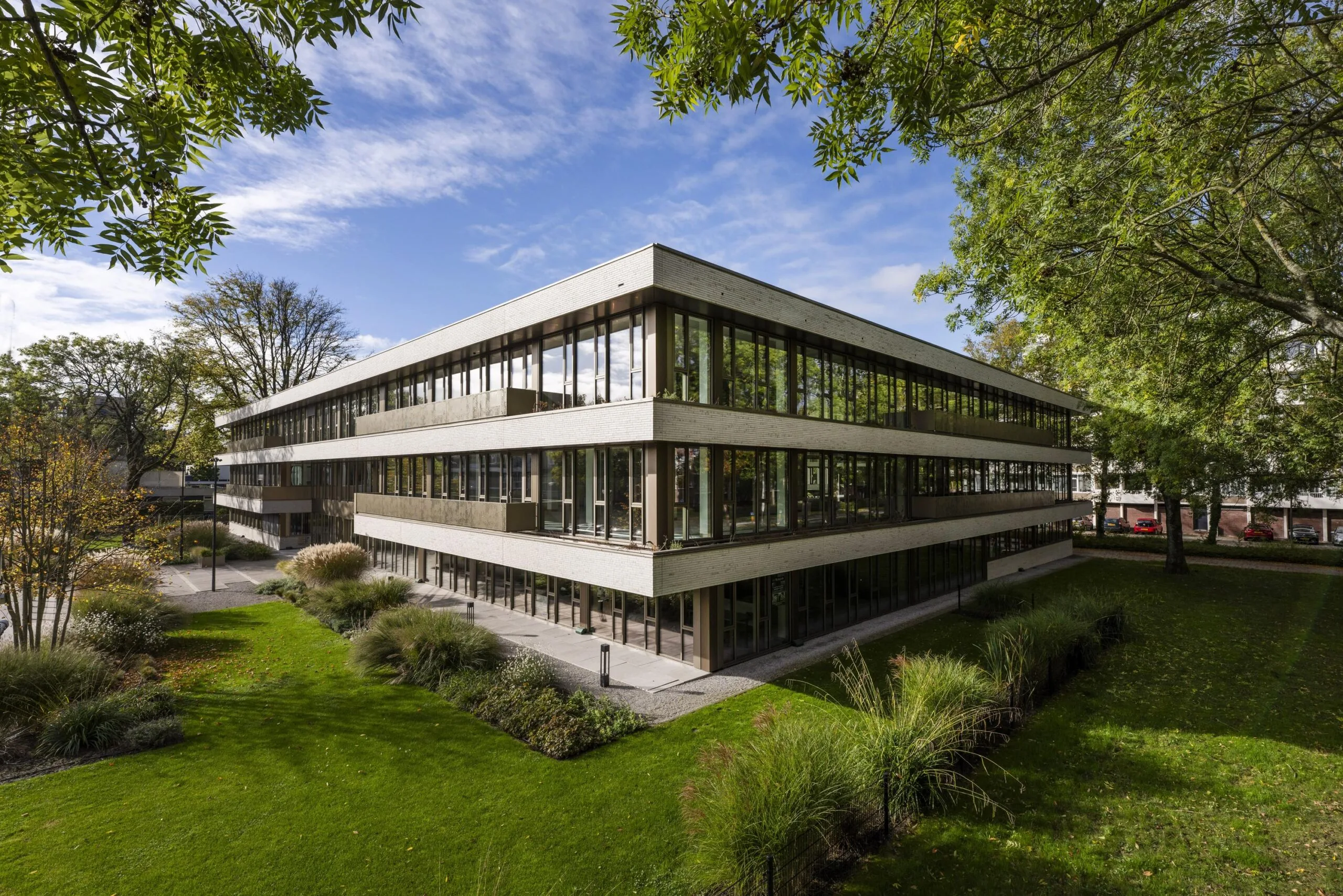 Modern three-story office building 'Walborg' surrounded by greenery and trees under a partly cloudy sky.