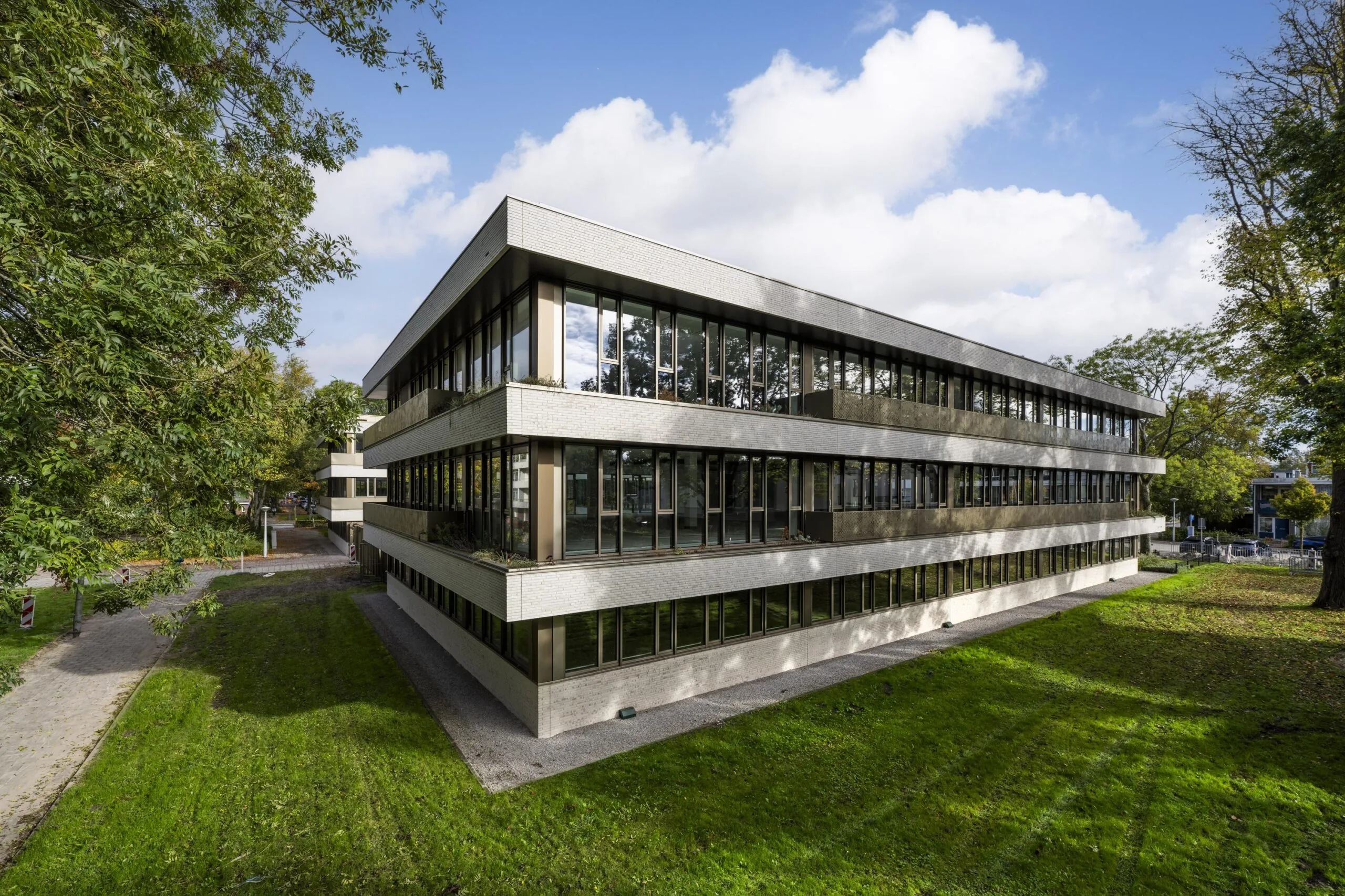 Modern three-story office building "Walborg" with large windows, surrounded by green grass and trees under a partly cloudy sky.