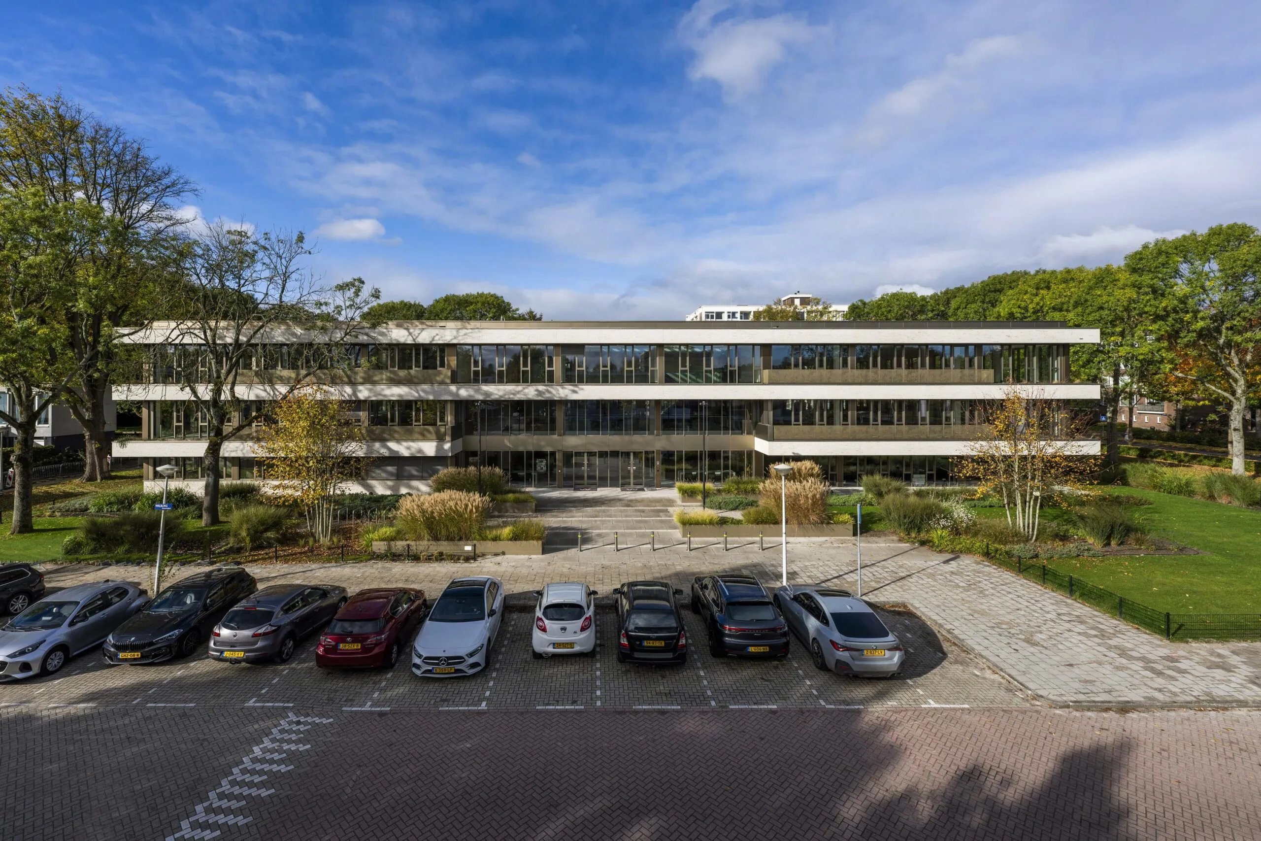 Modern office building Walborg 2 in Amsterdam surrounded by greenery with parked cars in front.