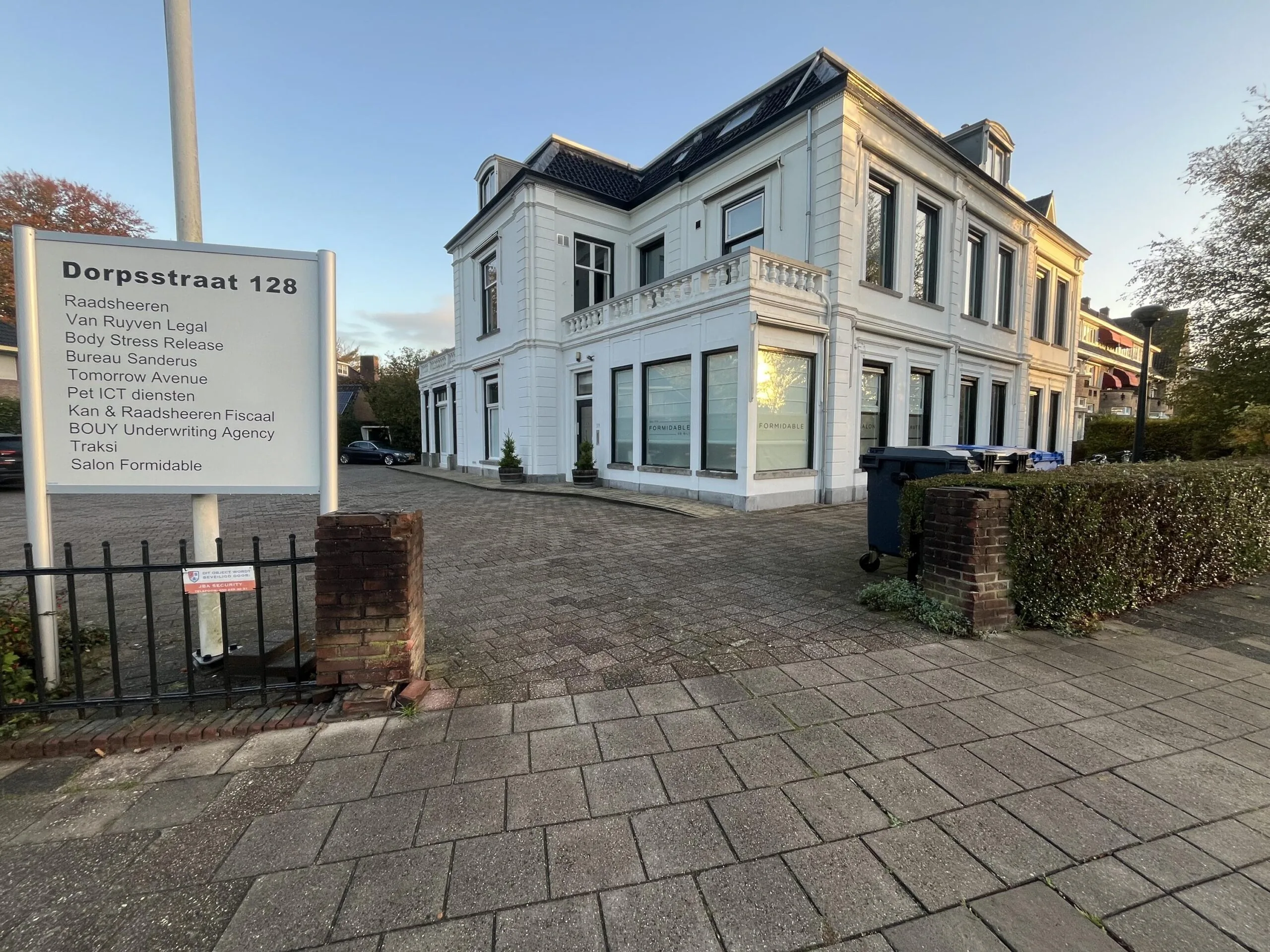 White office building at Dorpsstraat 128 with a sign listing multiple businesses at the entrance.