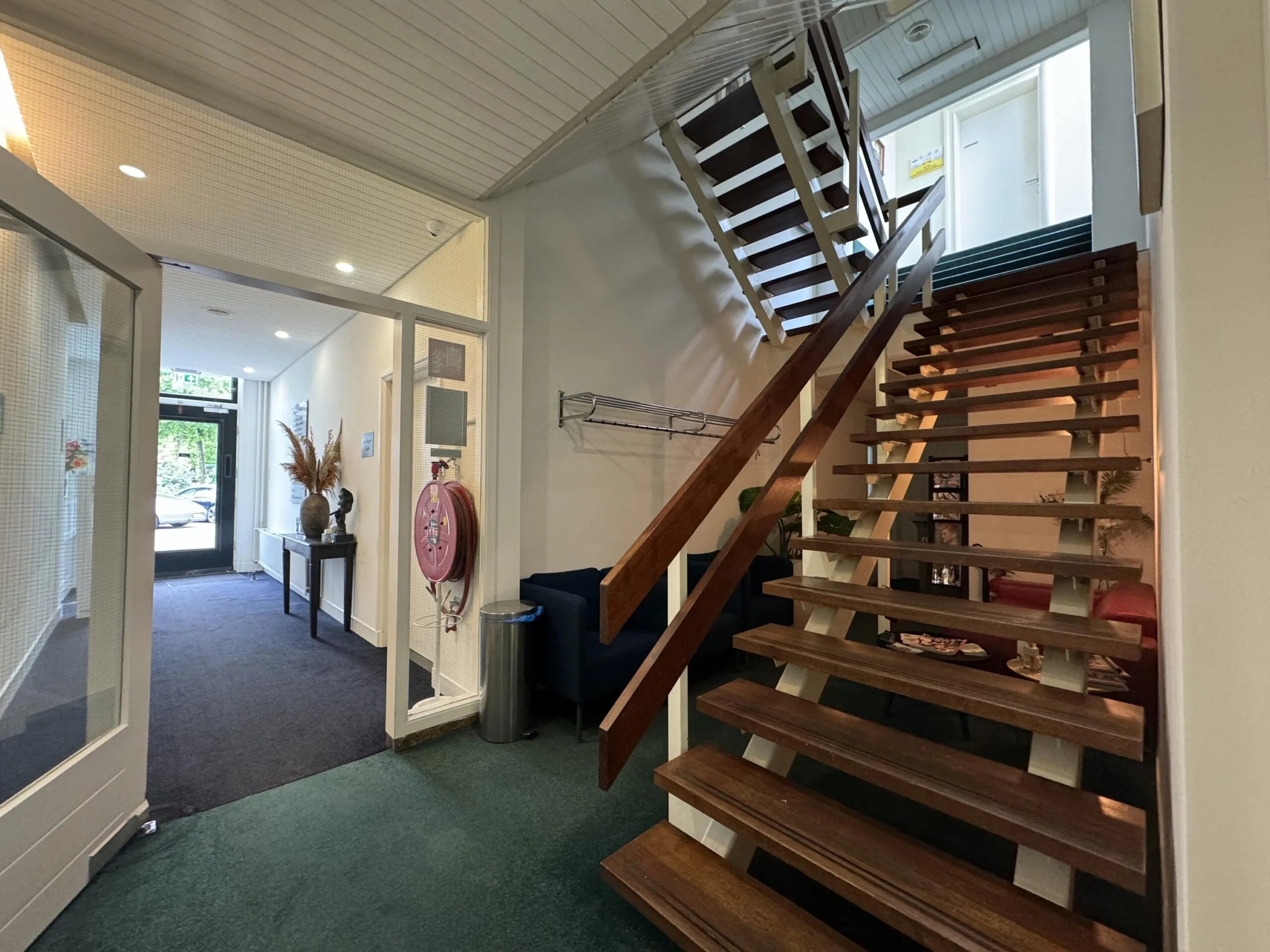 Interior hallway of a building on Dorpsstraat near Steenstraat with a wooden staircase and a glass entrance door.