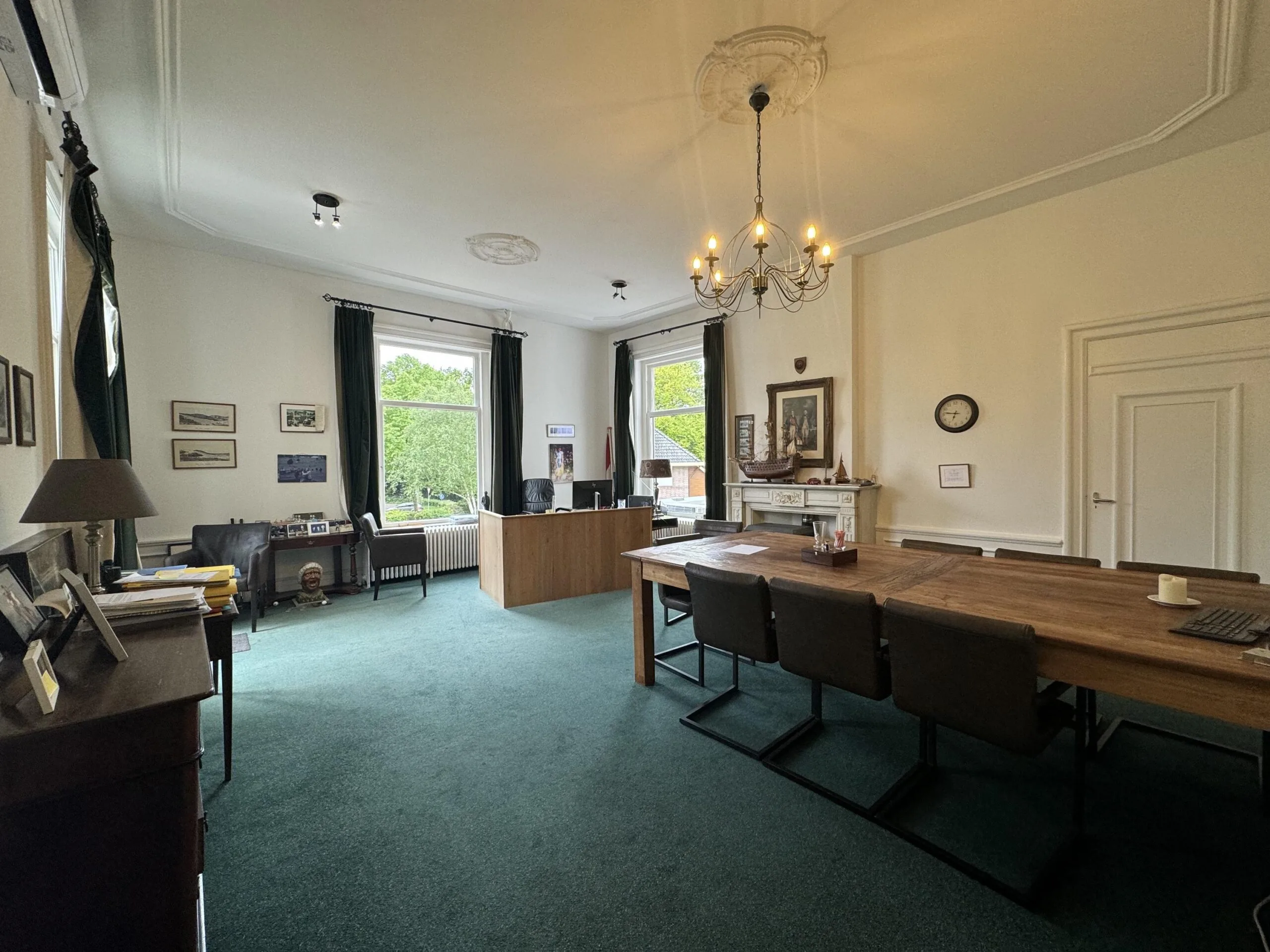 A spacious and elegant office with large windows, a wooden meeting table, and a desk overlooking Dorpsstraat near Steenstraat.
