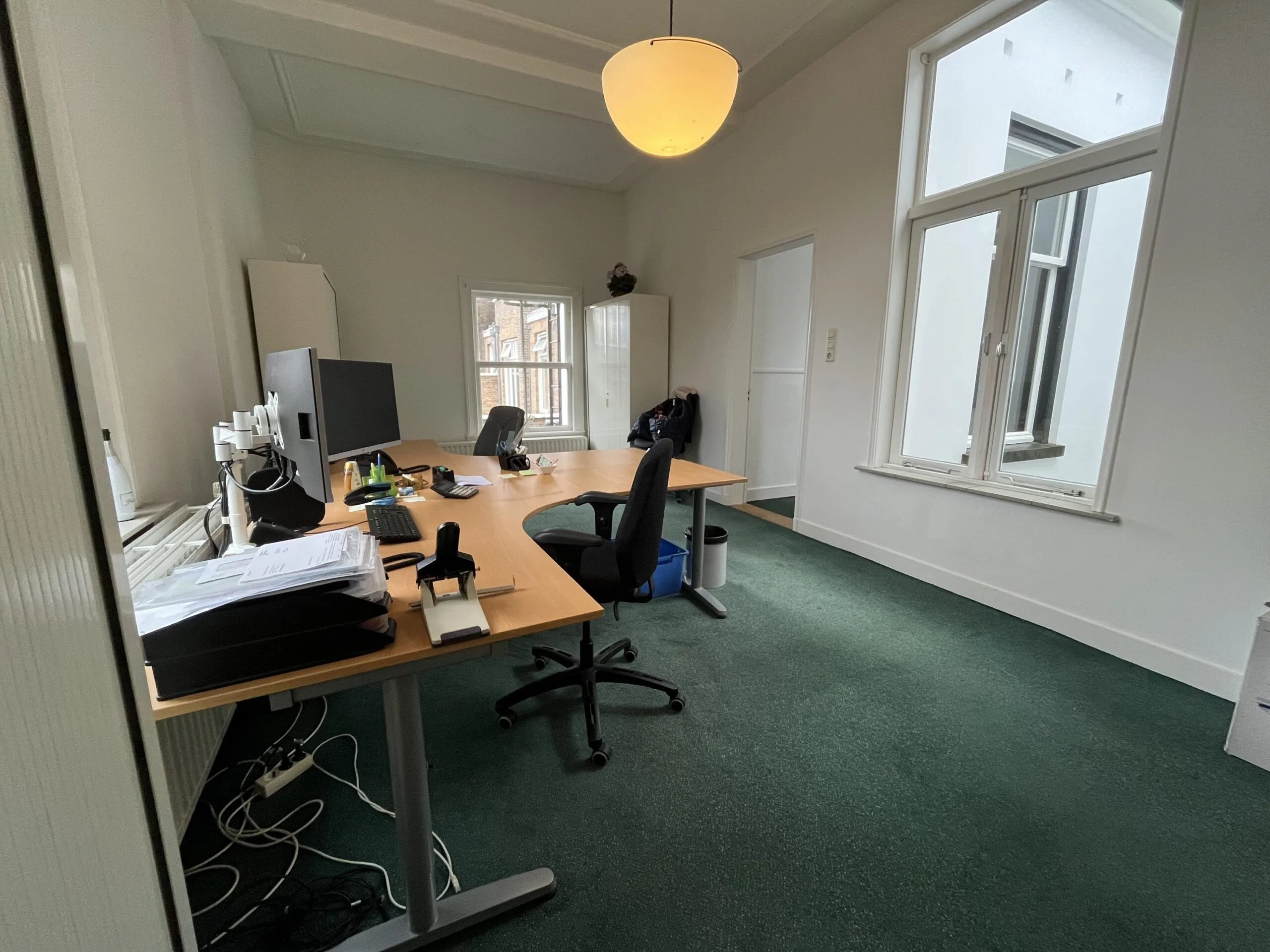 A modern office space on Dorpsstraat near Steenstraat with two desks, computer monitors, and large windows providing natural light.