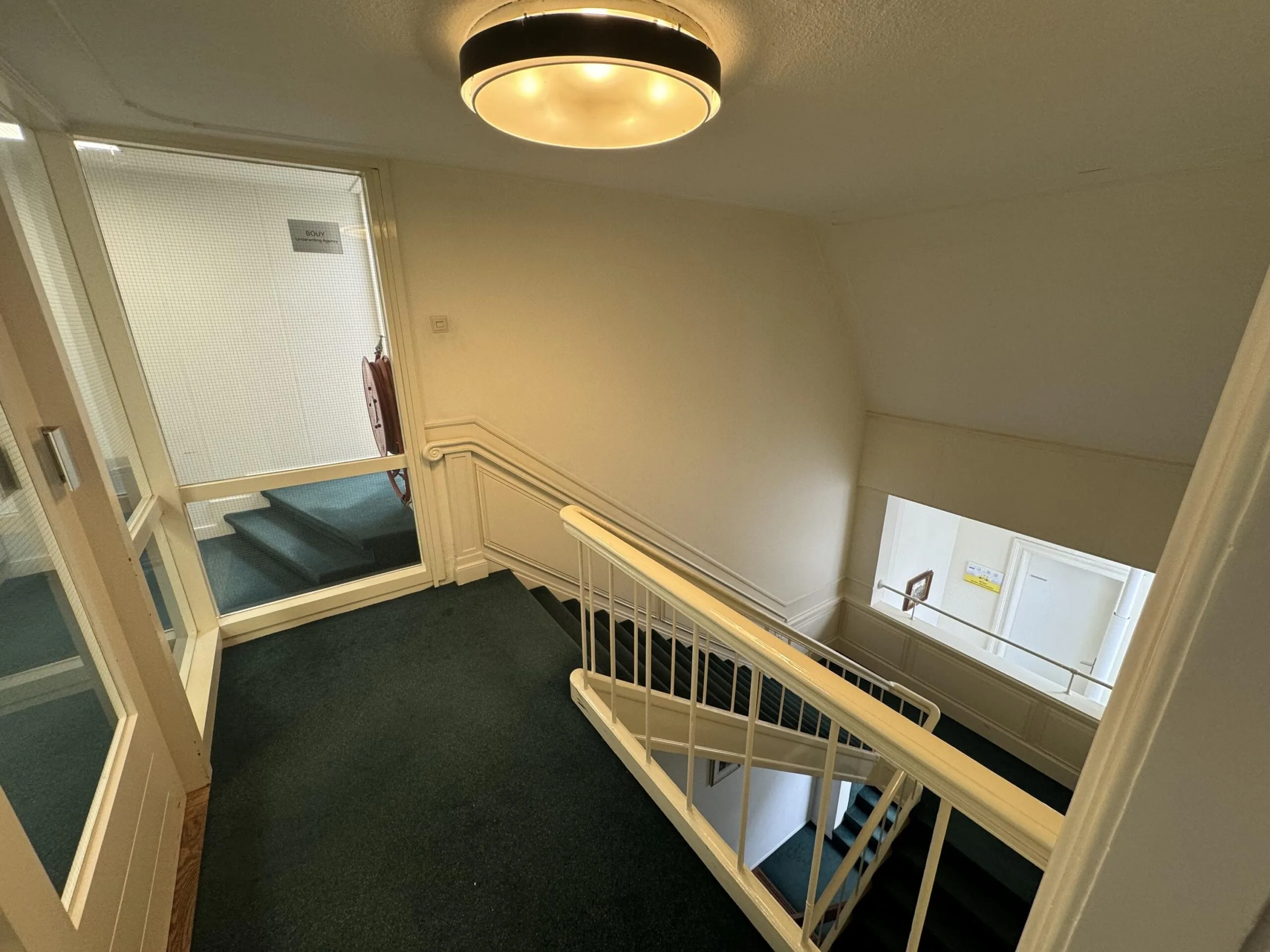 Interior view of a stairwell and hallway in a building on Dorpsstraat near Steenstraat, with white walls and green carpet.