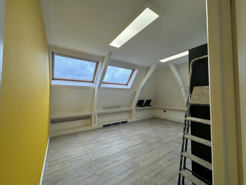 Bright attic room on Dorpsstraat with two skylights, a yellow accent wall, and a ladder, appearing to be under renovation.