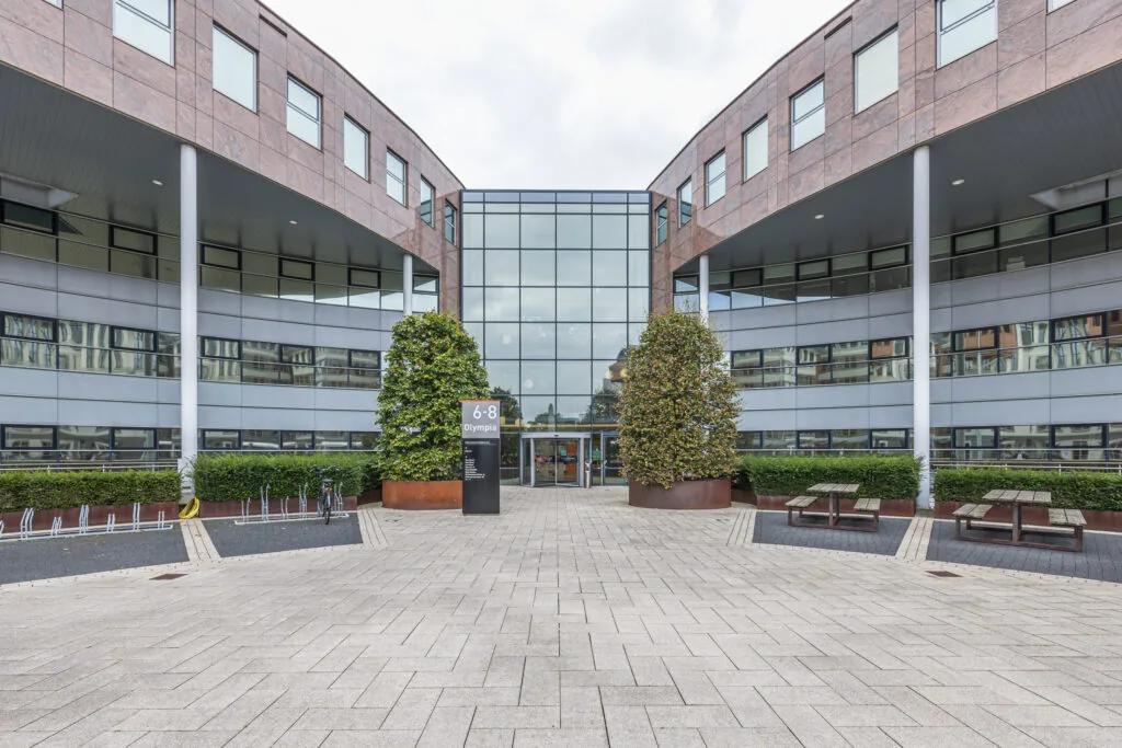 Modern office building named Olympia located at number 6-8, with a glass entrance, symmetrical architecture, and outdoor seating and bike racks.