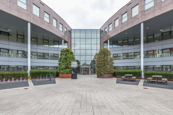 Modern office building named Olympia located at number 6-8, with a glass entrance, symmetrical architecture, and outdoor seating and bike racks.