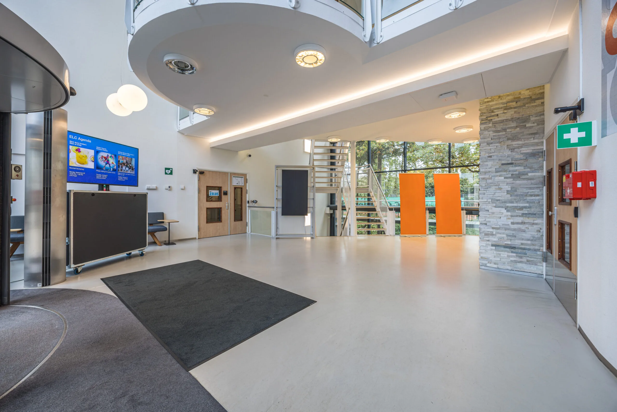 Modern reception area of the Olympia building with clean design, digital signage, and a staircase leading to the upper floor.