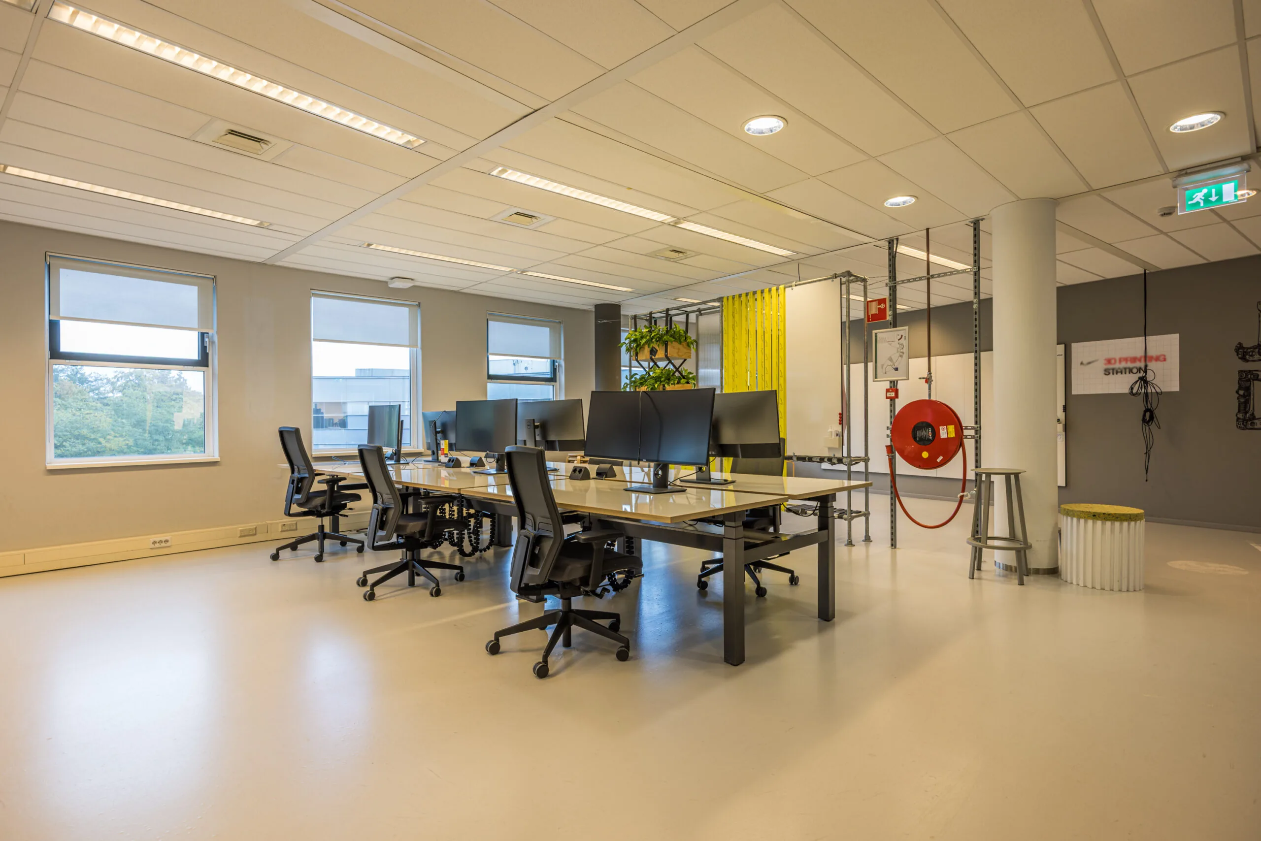 Modern open office workspace with multiple desks, ergonomic chairs, and large monitors, located in the Olympia building.