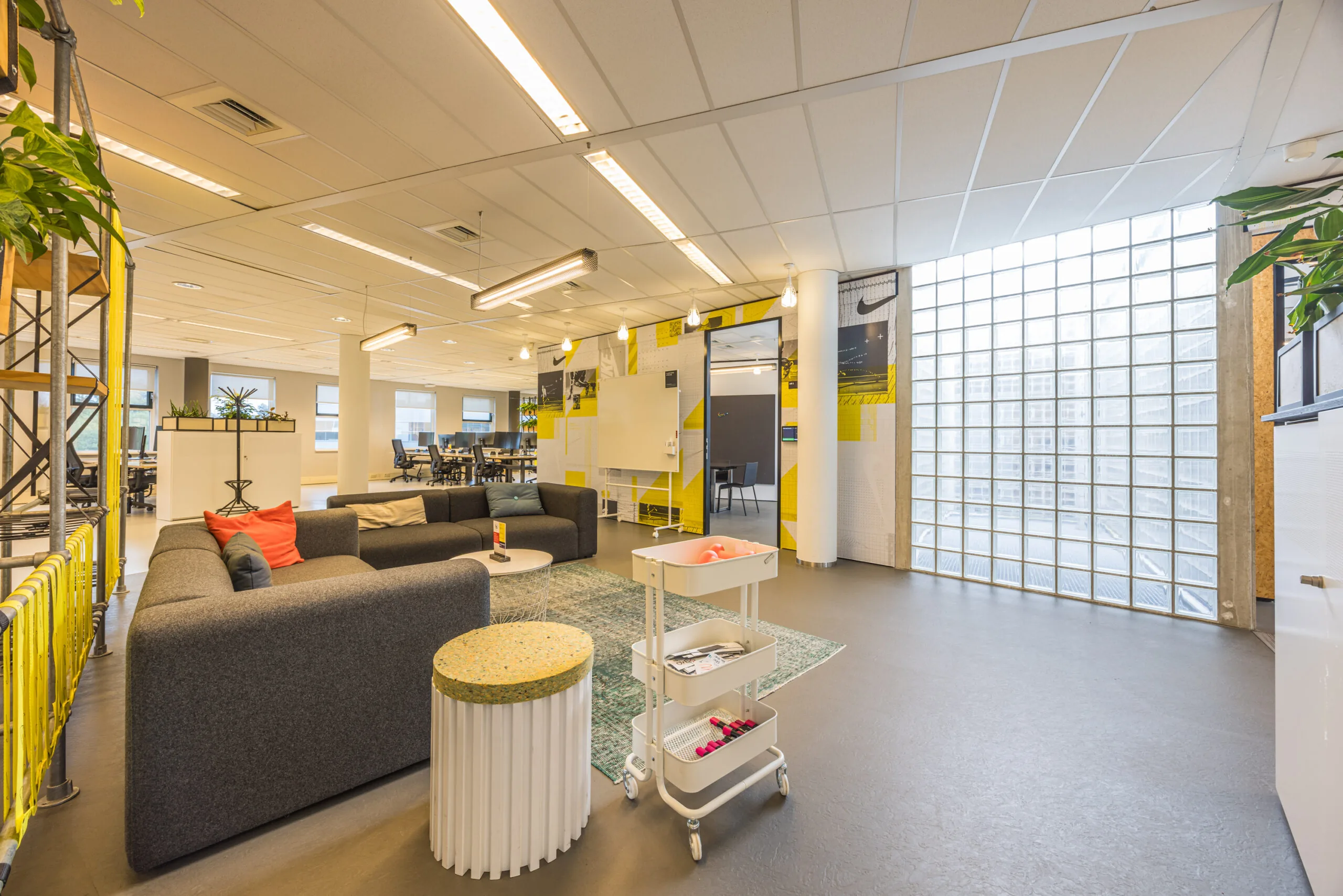 Modern office space at Olympia with lounge seating, a mobile cart, and a large glass block window providing natural light.