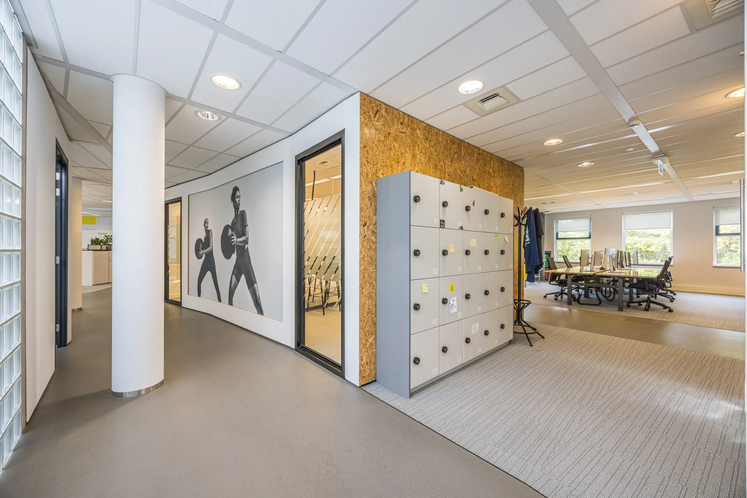 Modern office interior with lockers, a meeting room, and a wall mural of two athletes exercising.