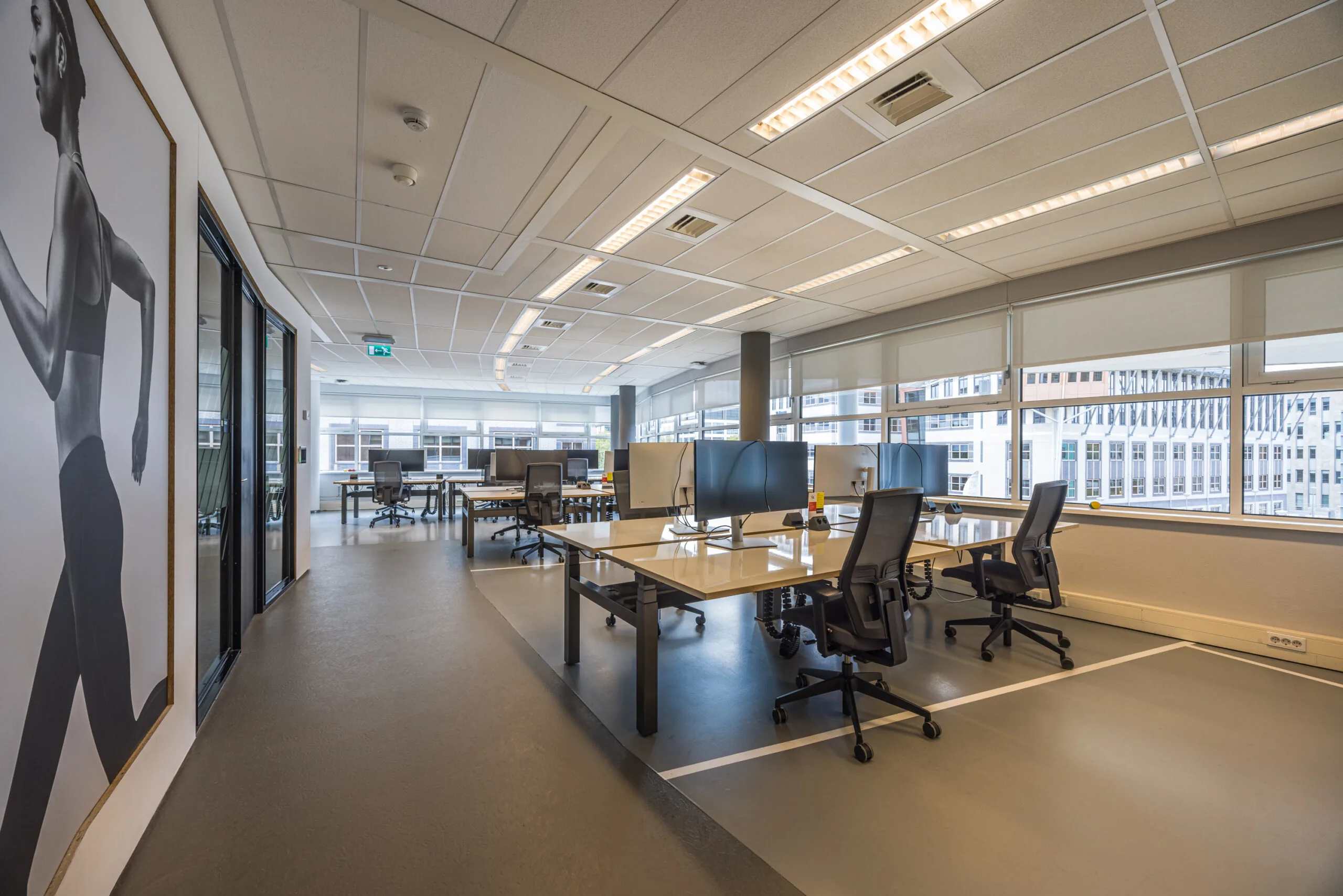 Modern open-plan office space at Olympia with multiple workstations, large windows, and a wall-sized photo of a runner.