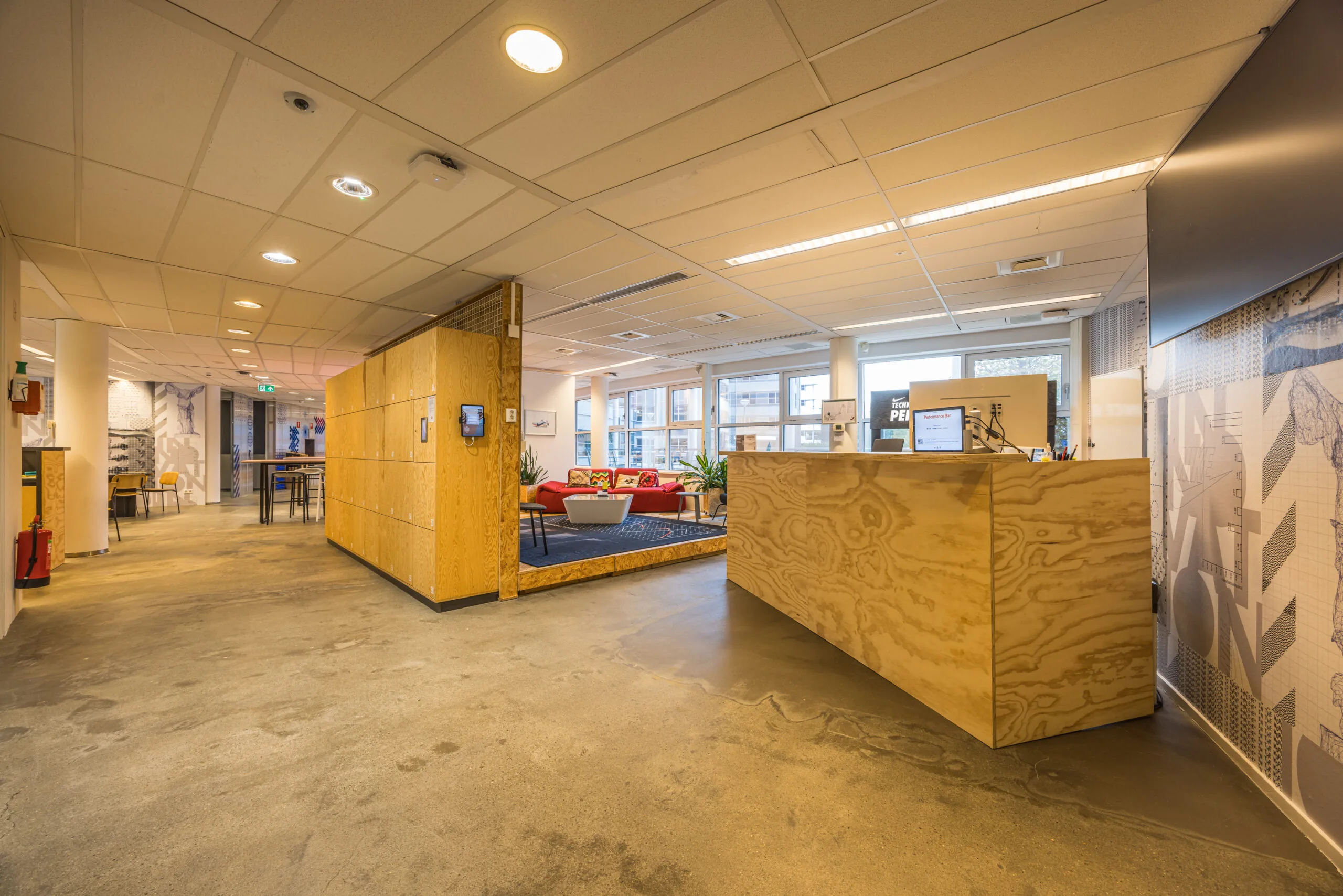 Modern office reception area with plywood furnishings, a cozy seating corner, and large windows letting in natural light.