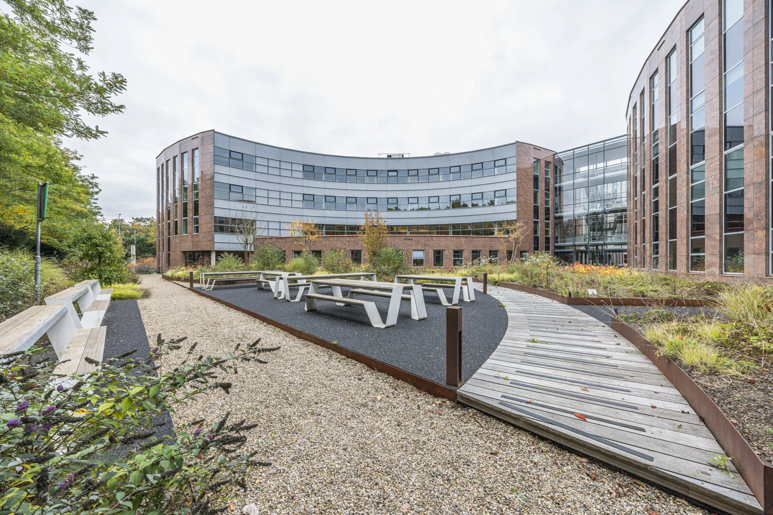 Modern office building Olympia with curved glass facade and landscaped outdoor seating area with benches and walking paths.
