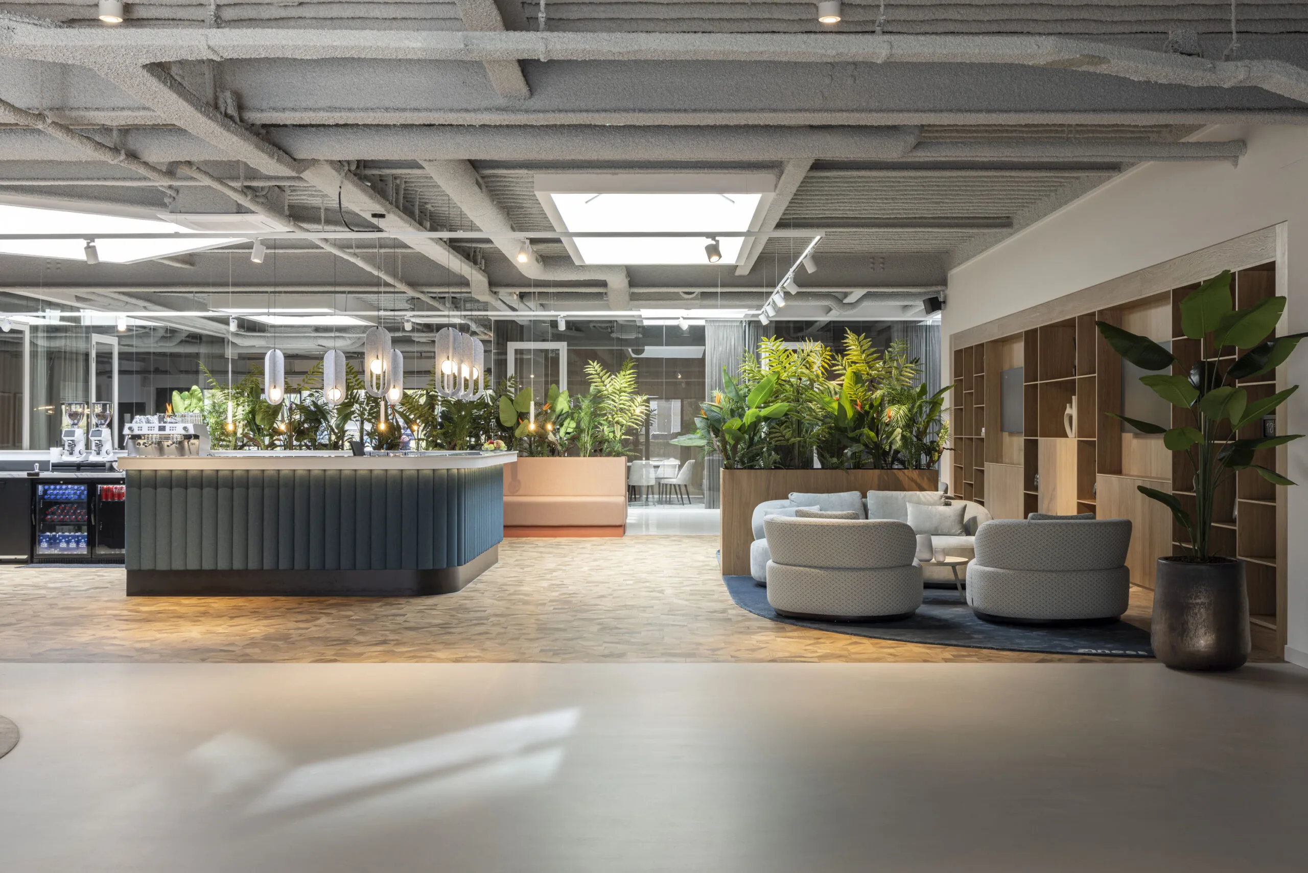 Modern office lobby with a central coffee bar, stylish seating area, and abundant green plants.