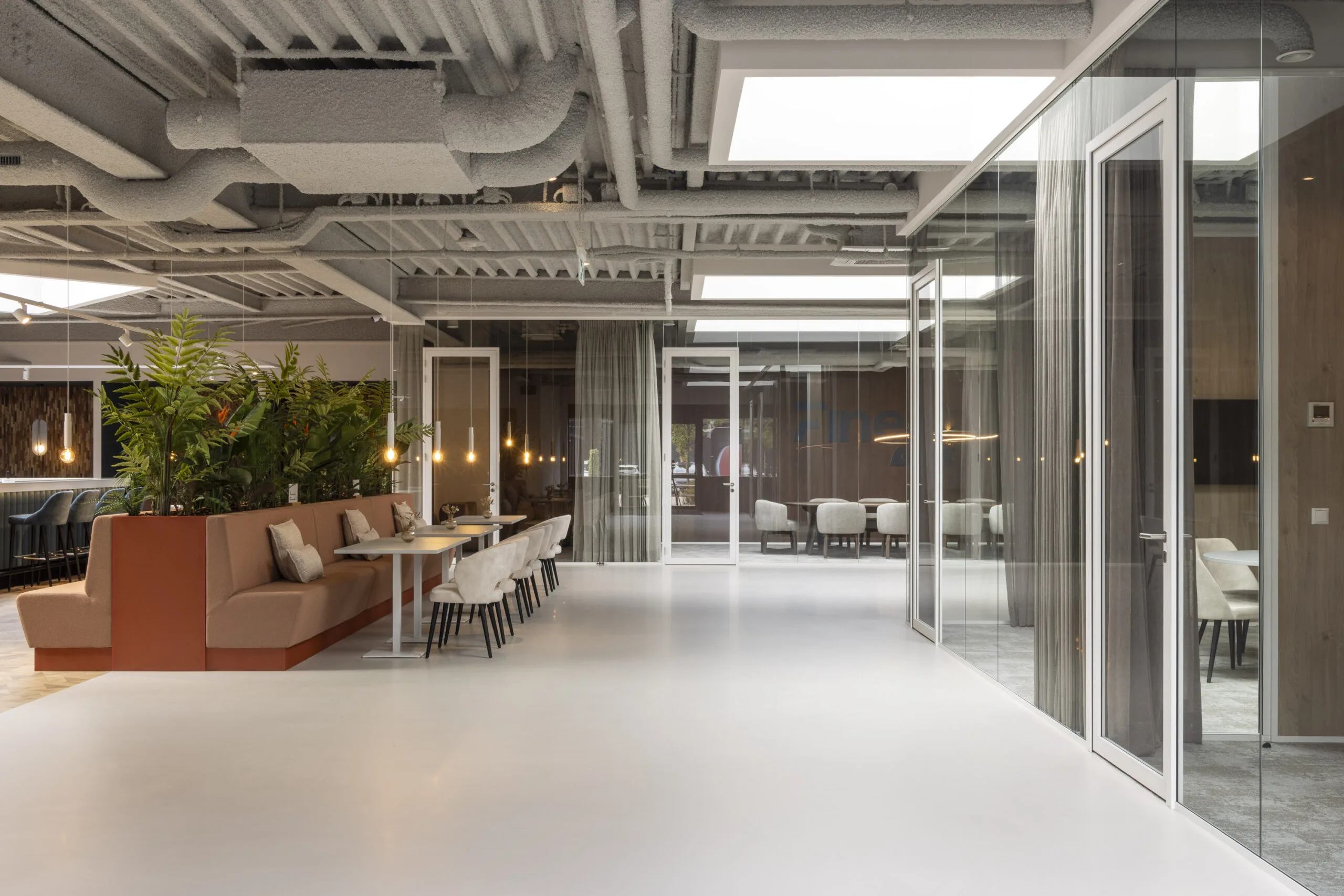Modern office interior with open seating area, glass-walled meeting rooms, and ceiling with exposed ductwork.