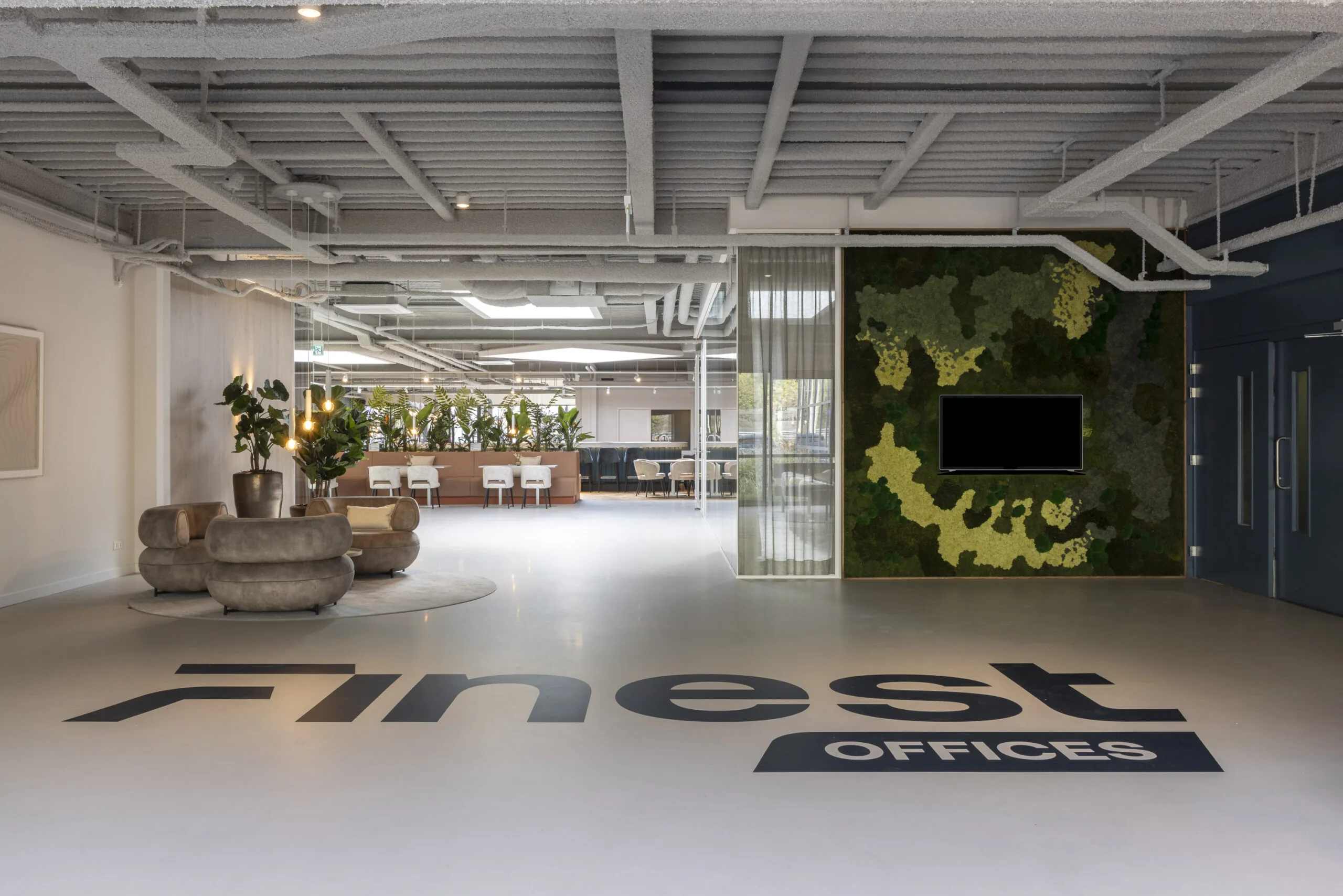 Modern office lobby of "Finest Offices" at Essebaan, featuring stylish seating, a vertical green wall, and an open workspace in the background.