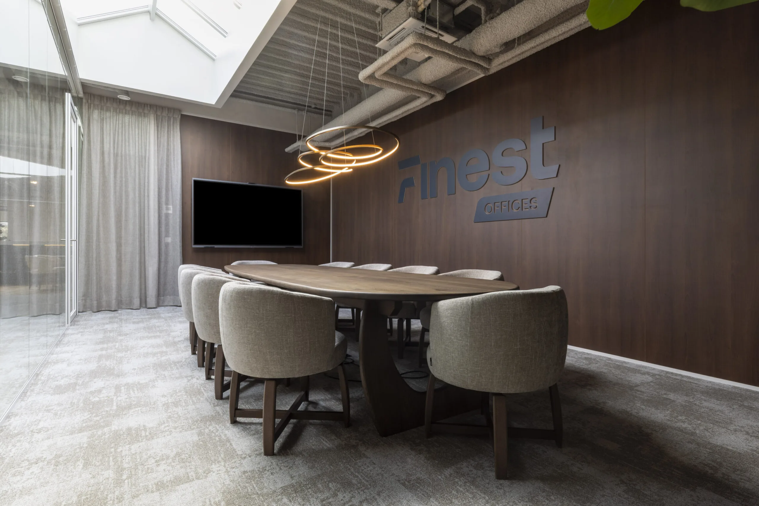 Modern conference room at Finest Offices featuring a large wooden table, beige chairs, ring-shaped pendant lights, and a wall-mounted screen.
