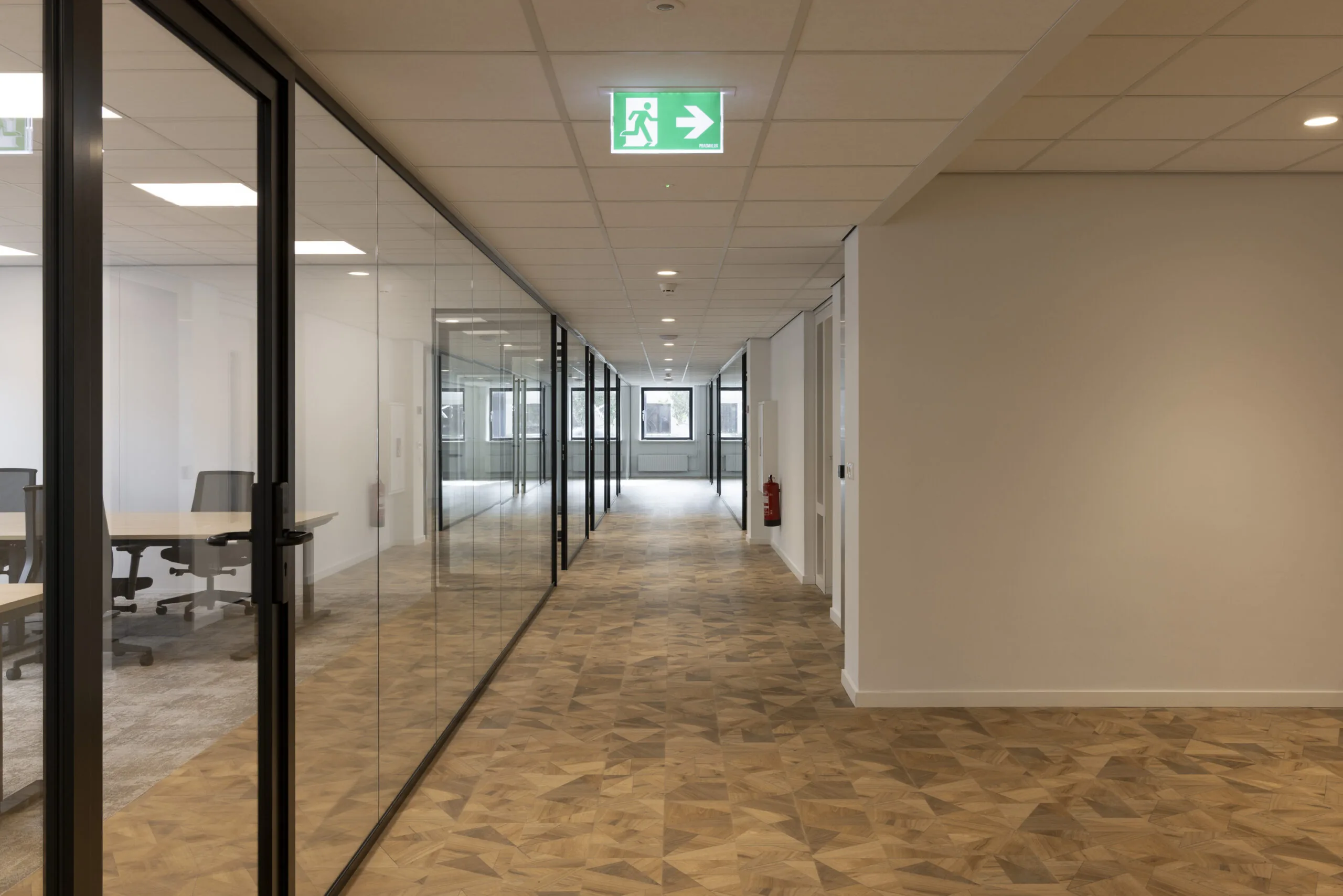 Modern office hallway at Essebaan with glass-walled meeting rooms and a visible emergency exit sign.