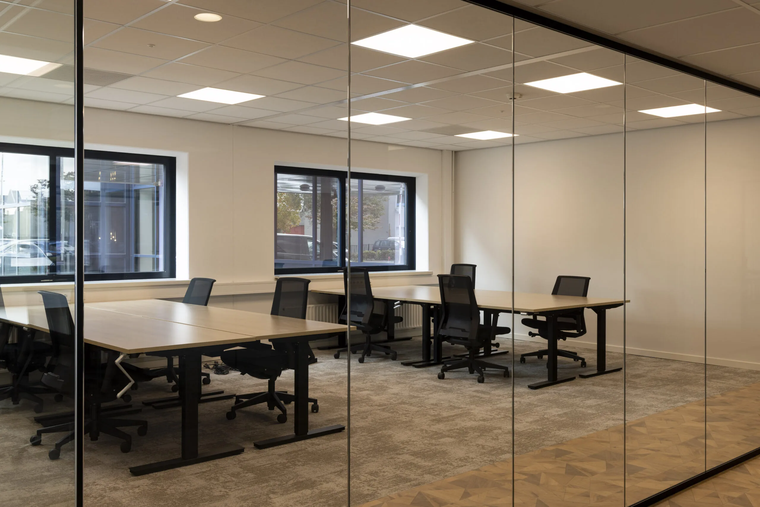 Modern office space on Essebaan with multiple desks and ergonomic chairs seen through a glass wall.