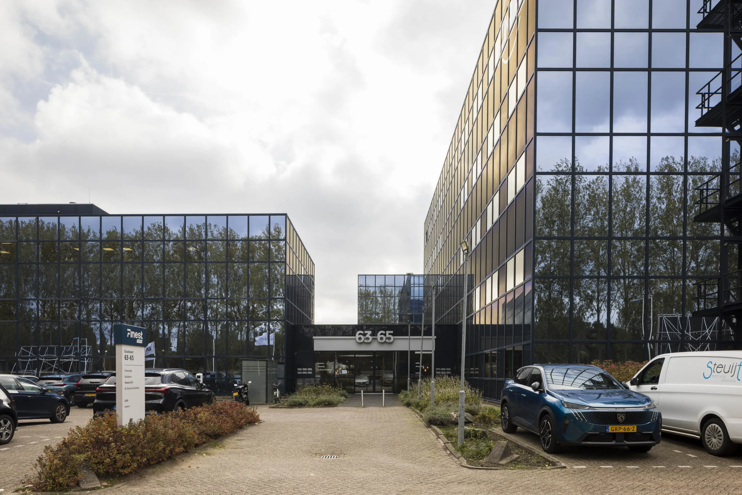 Modern office building at Essebaan 63-65 with mirrored glass facade and parked cars in front.