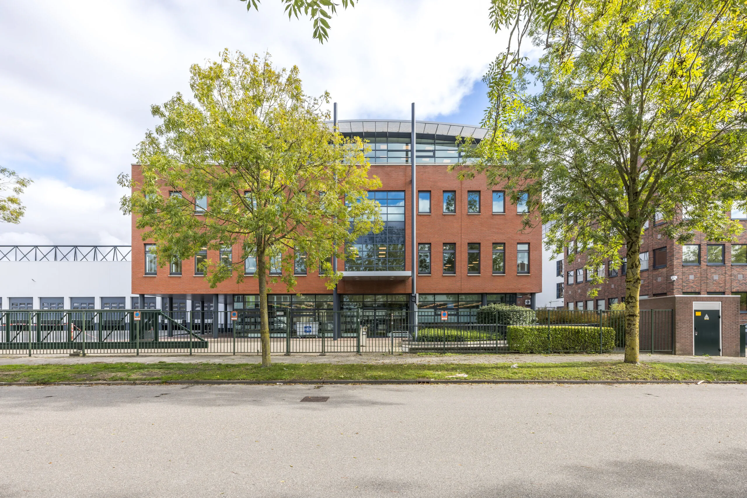 Modern office building named “Veldzigt” with a red-brick facade, large windows, and trees in front.