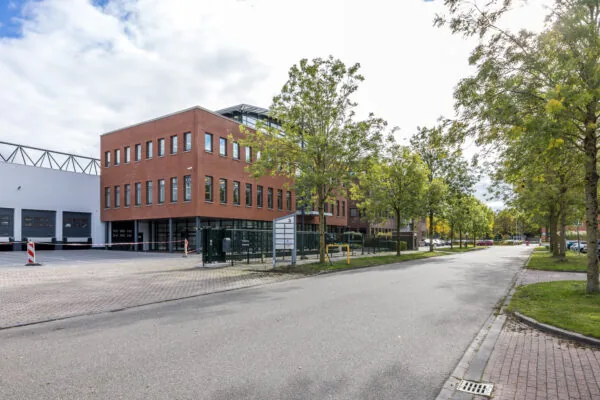 Modern office and industrial building on Veldzigt street surrounded by trees and parked cars.
