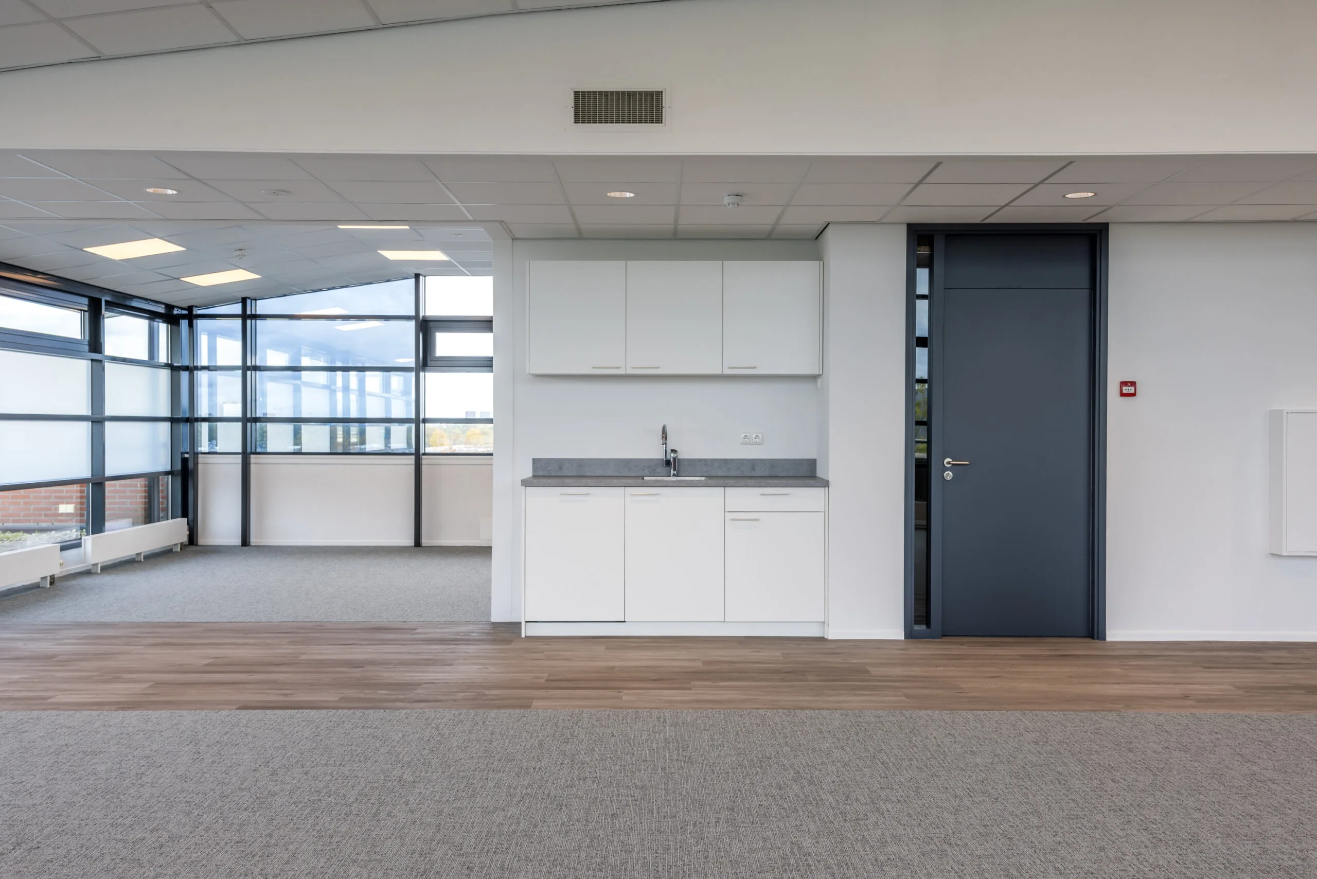 Modern office space with a small kitchenette and large windows providing natural light.