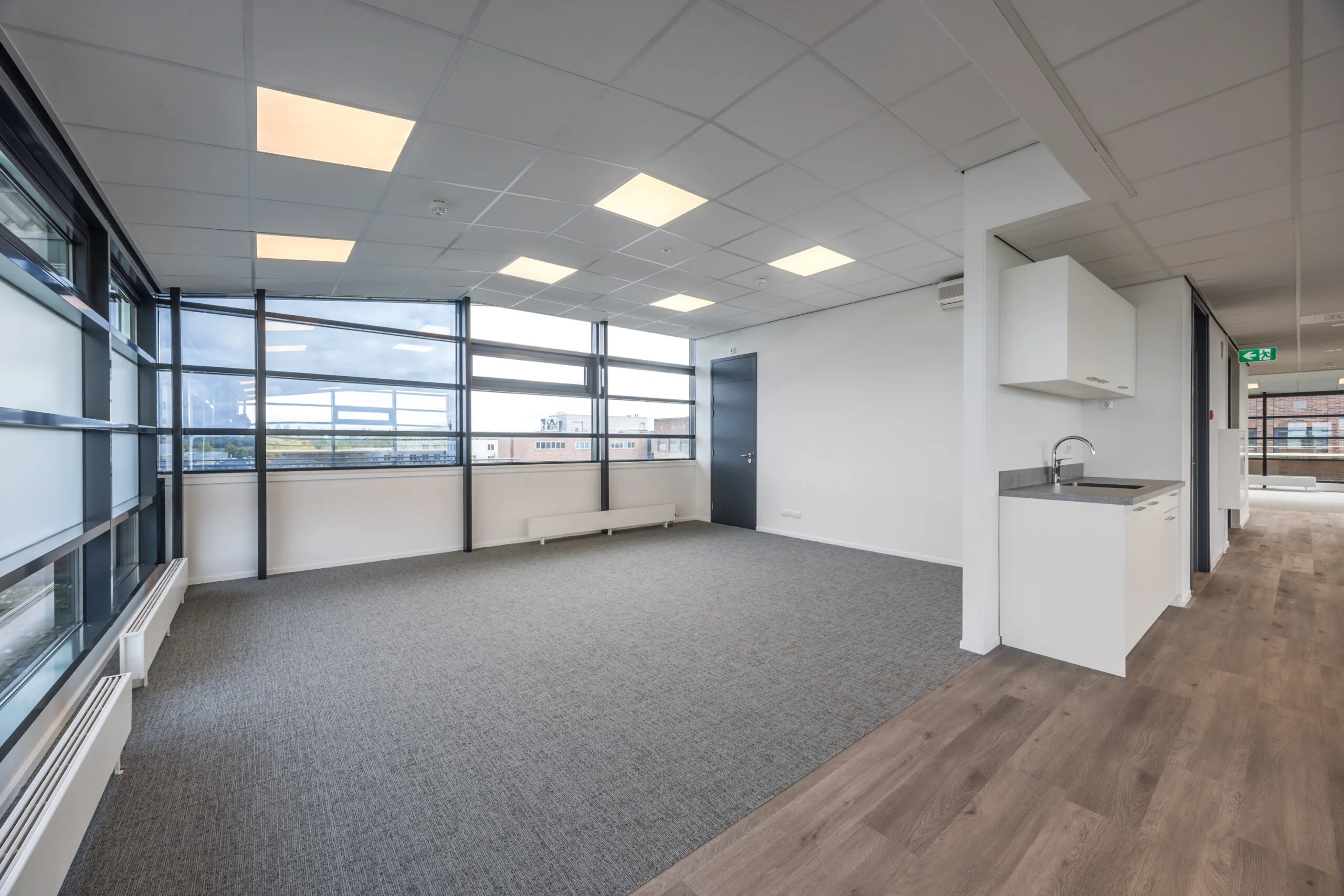 Modern, unfurnished office space at Veldzigt with large windows, carpeted flooring, and a kitchenette.