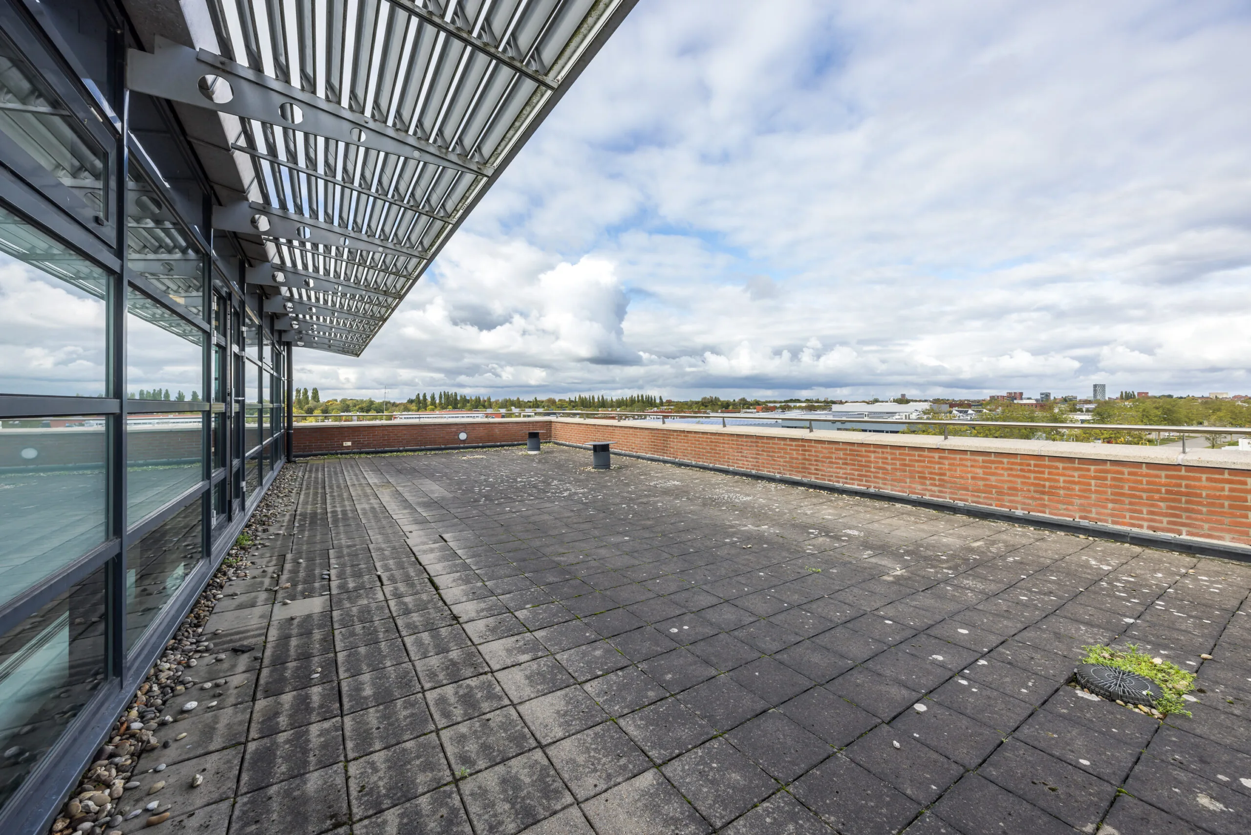 Spacious rooftop terrace with tiled flooring, partial glass facade, and a wide view over the surrounding area in Veldzigt.