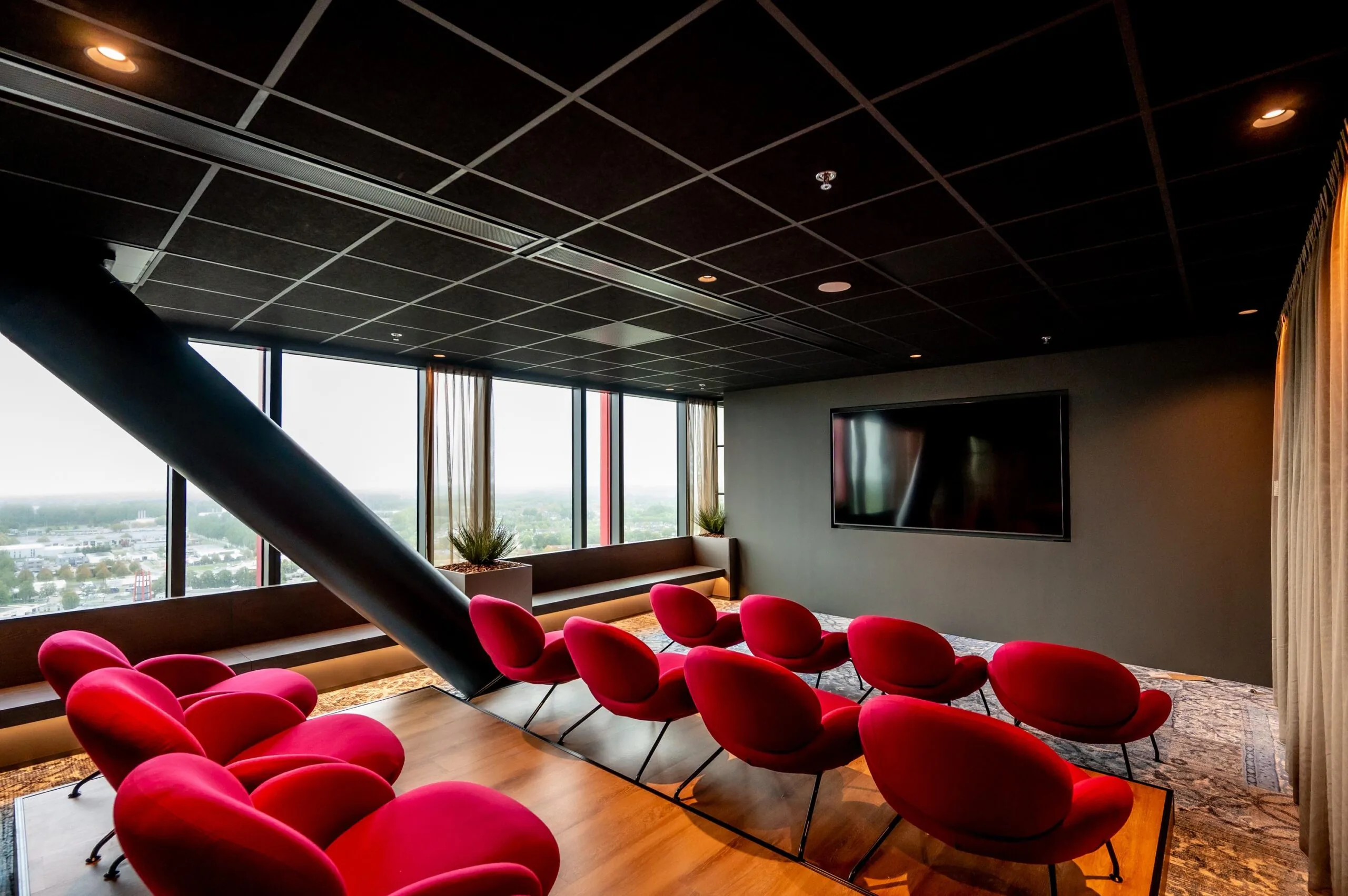 Modern presentation room on P.J. Oudweg with red chairs, a large screen, and panoramic windows offering a city view.