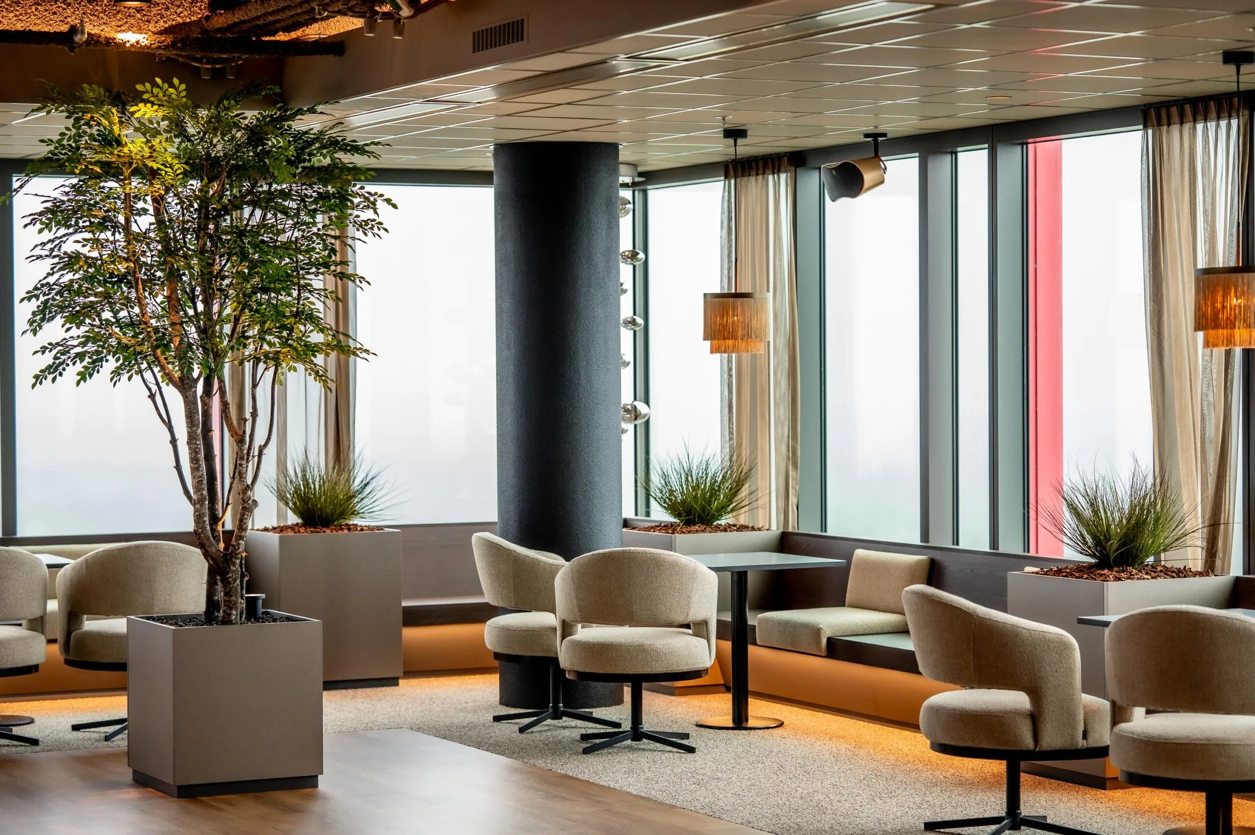 Modern lounge area at P.J. Oudweg with neutral-toned seating, large windows, and indoor plants.