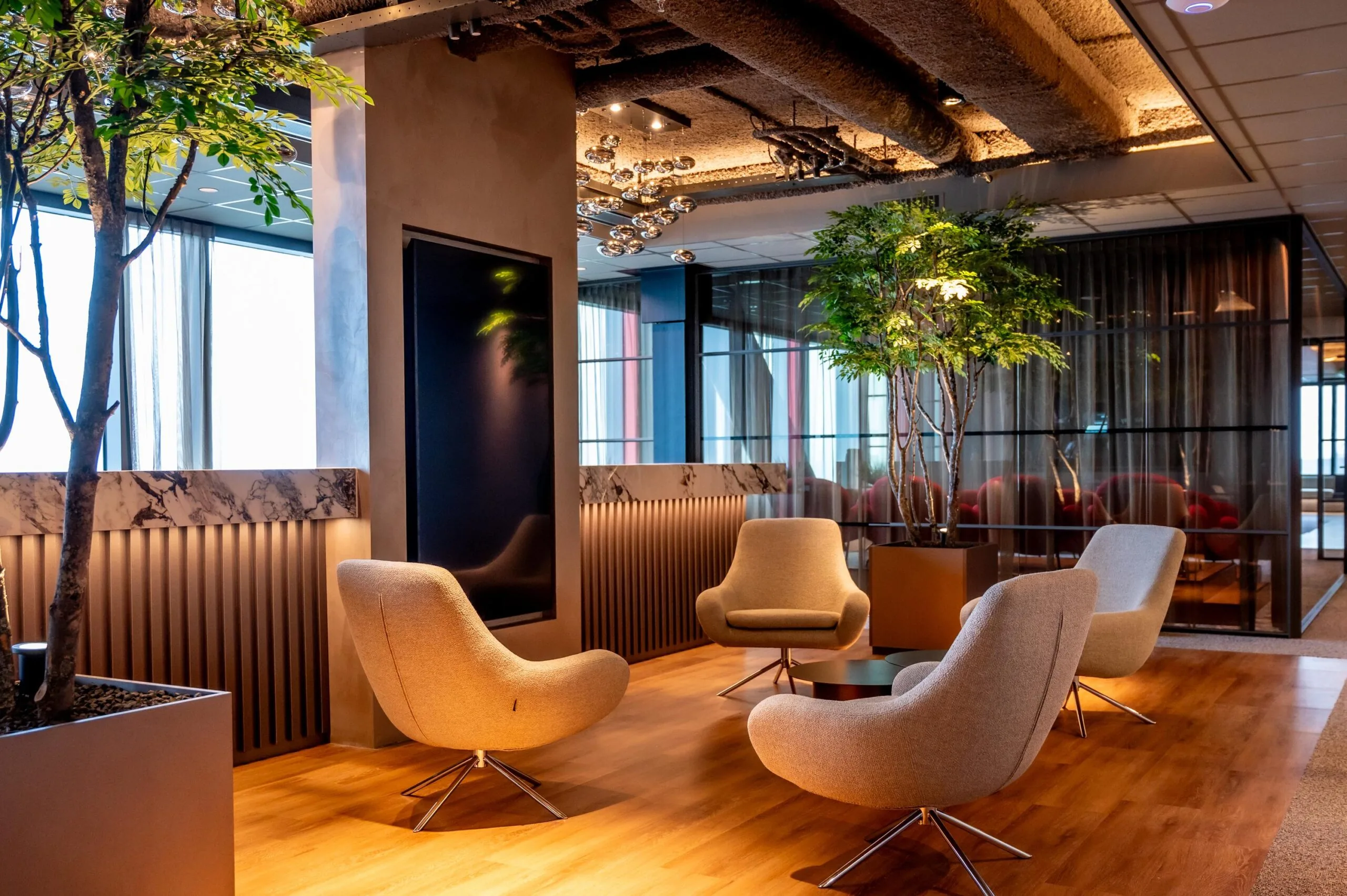 Modern lounge area at P.J. Oudweg with stylish chairs, indoor trees, and warm lighting.