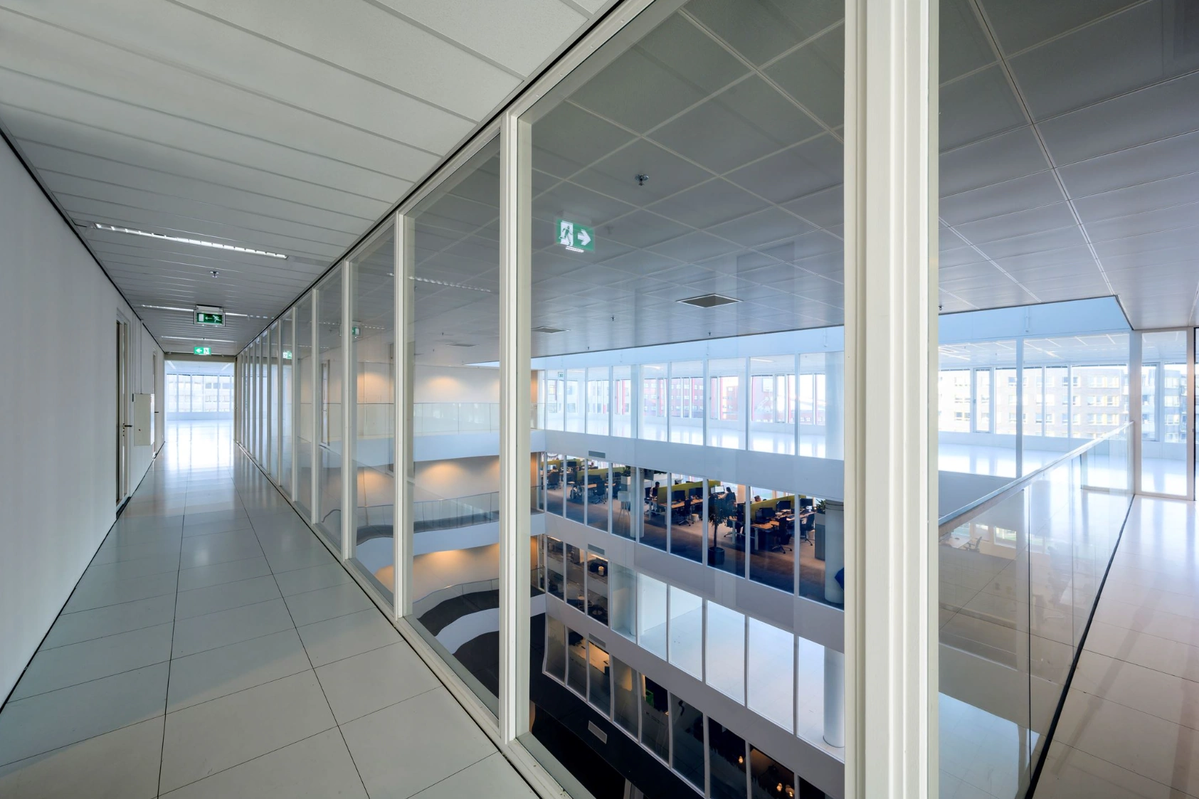 Modern office hallway with glass walls overlooking multiple floors of open-plan workspaces at P.J. Oudweg.