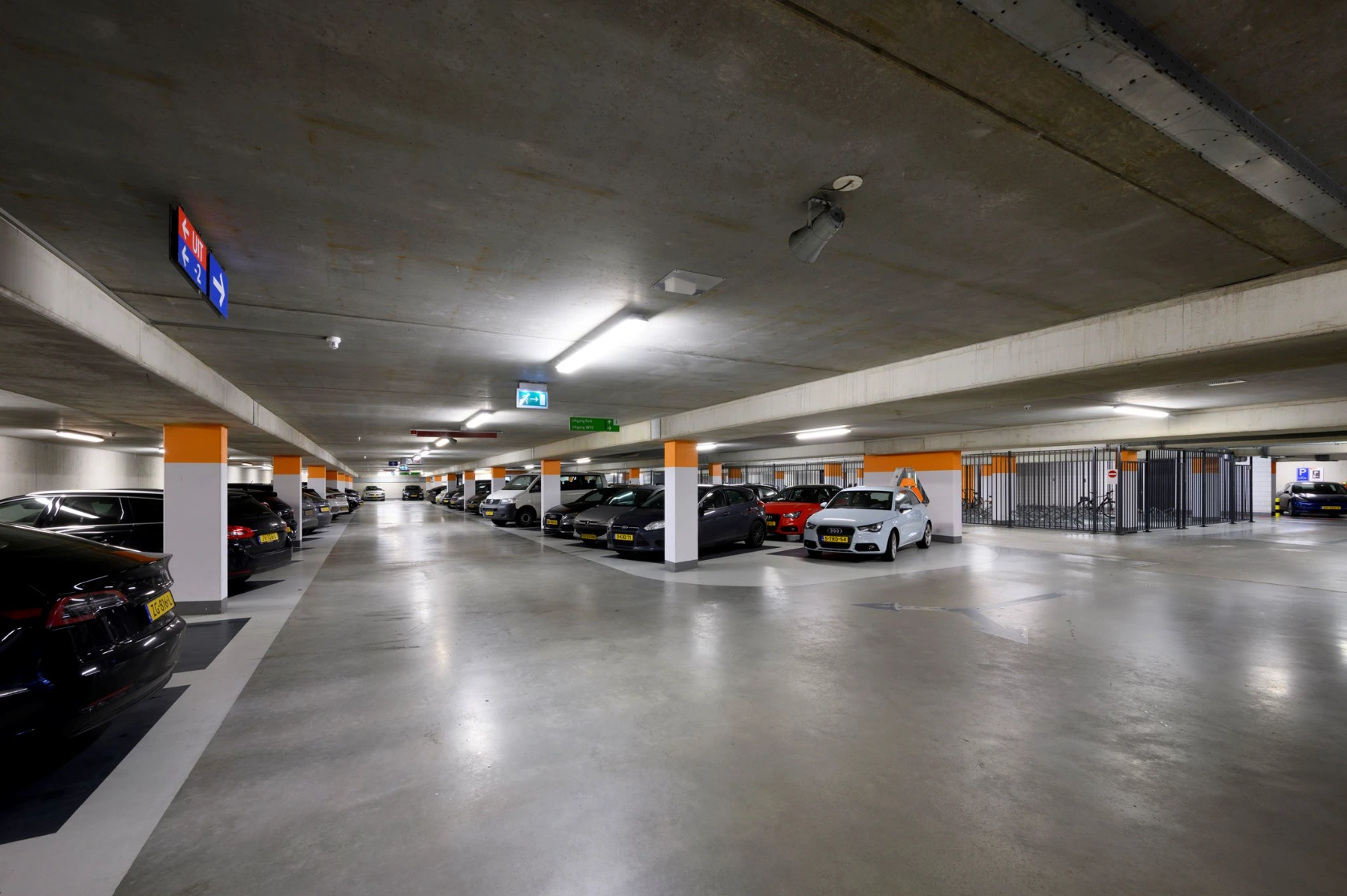 Underground parking garage at P.J. Oudweg with parked cars and gated bicycle storage area.