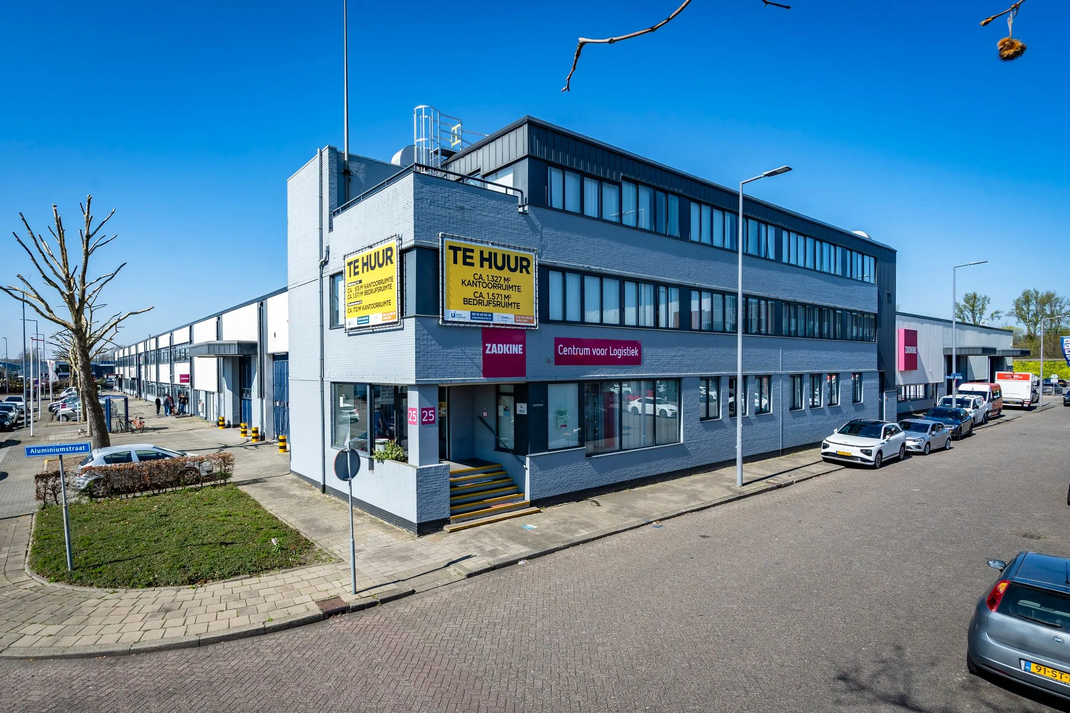 Gray commercial building on Aluminiumstraat with "For Rent" signs and a logistics training center.
