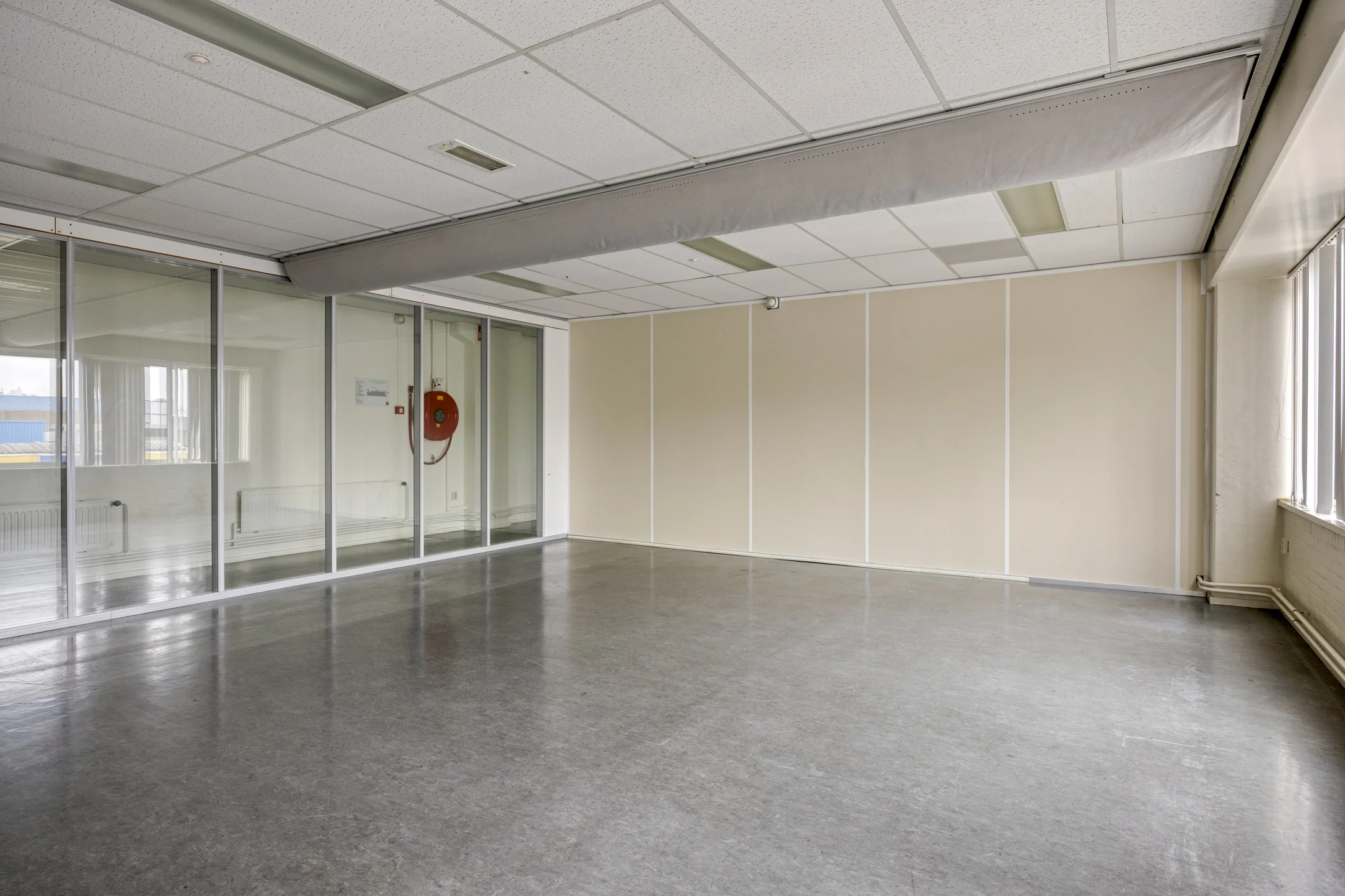 Empty office space on Aluminiumstraat with glass wall, beige partitions, and grey flooring.
