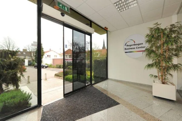Entrance area of the Regenbogen Business Center with glass doors, indoor plant, and outdoor view.